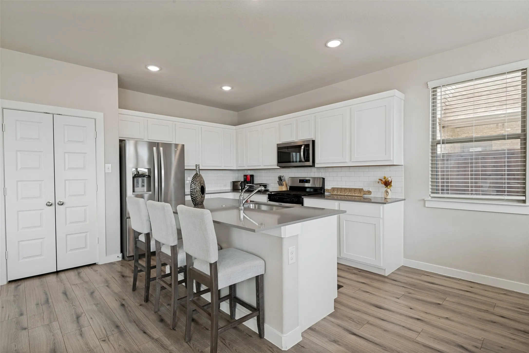 Kitchen featuring white cabinetry, solid-surface countertops, subway tile backsplash, stainless steel appliances, and wood-finish flooring