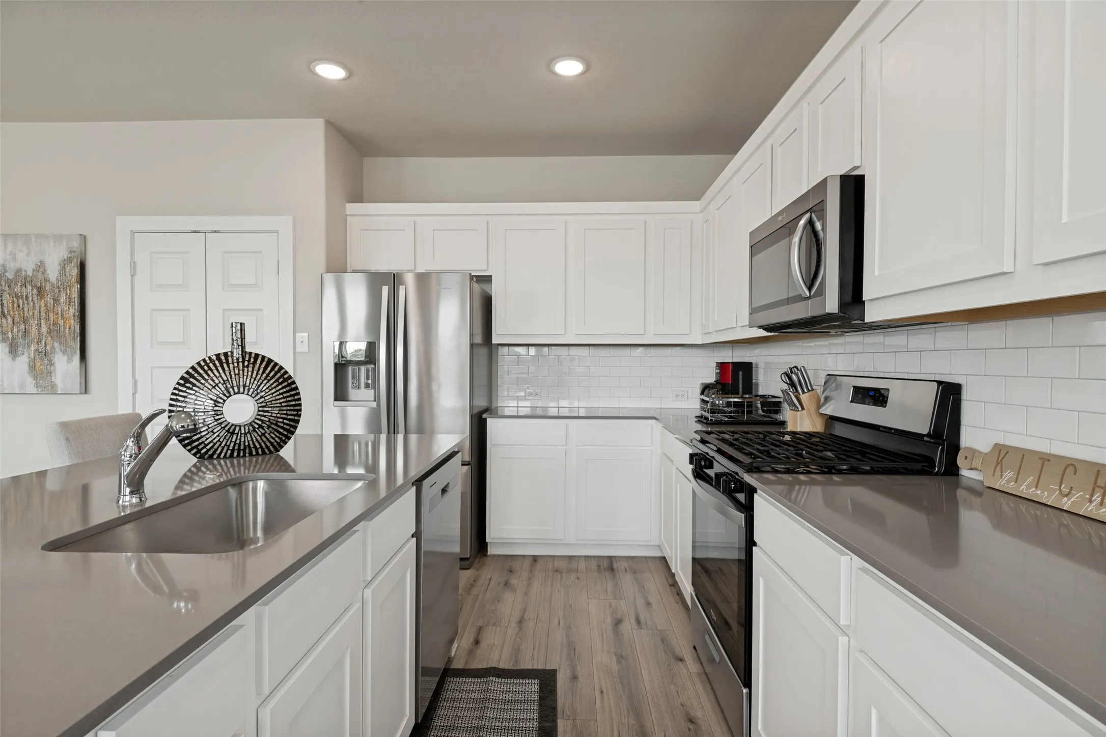 Kitchen featuring white Shaker-style cabinetry, quartz countertops, a white subway tile backsplash, stainless steel appliances, and wood-finish flooring
