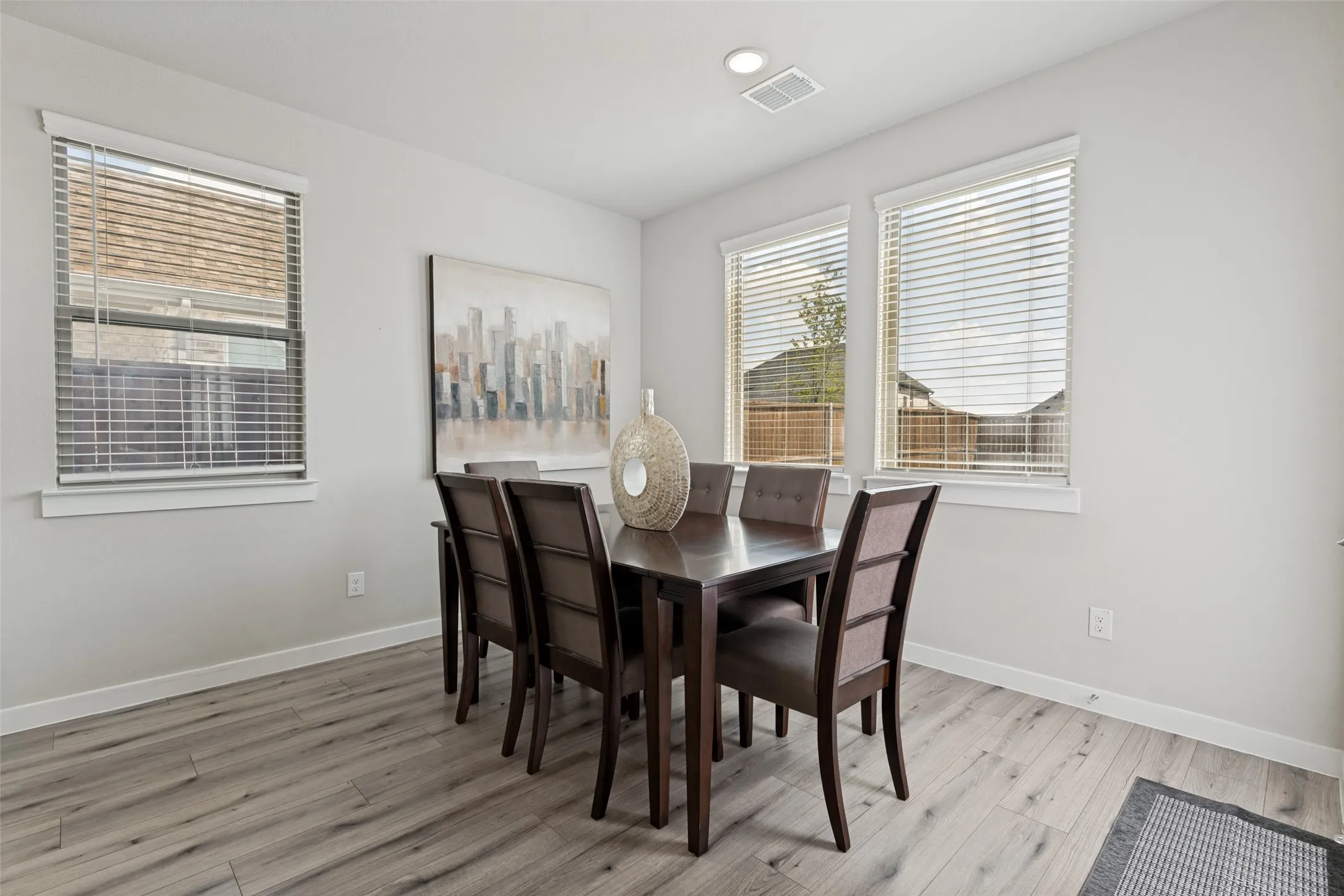 Neutral-toned interior space featuring wood-finish flooring, three windows with horizontal blinds, and recessed ceiling lighting