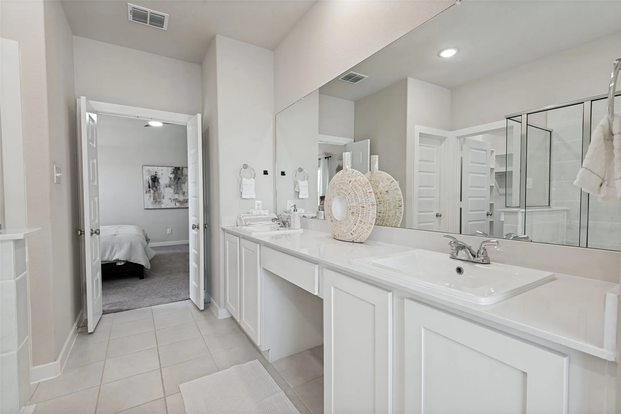 Double vanity featuring white cabinetry, a solid-surface countertop, dual drop-in sinks, and a full-width wall mirror