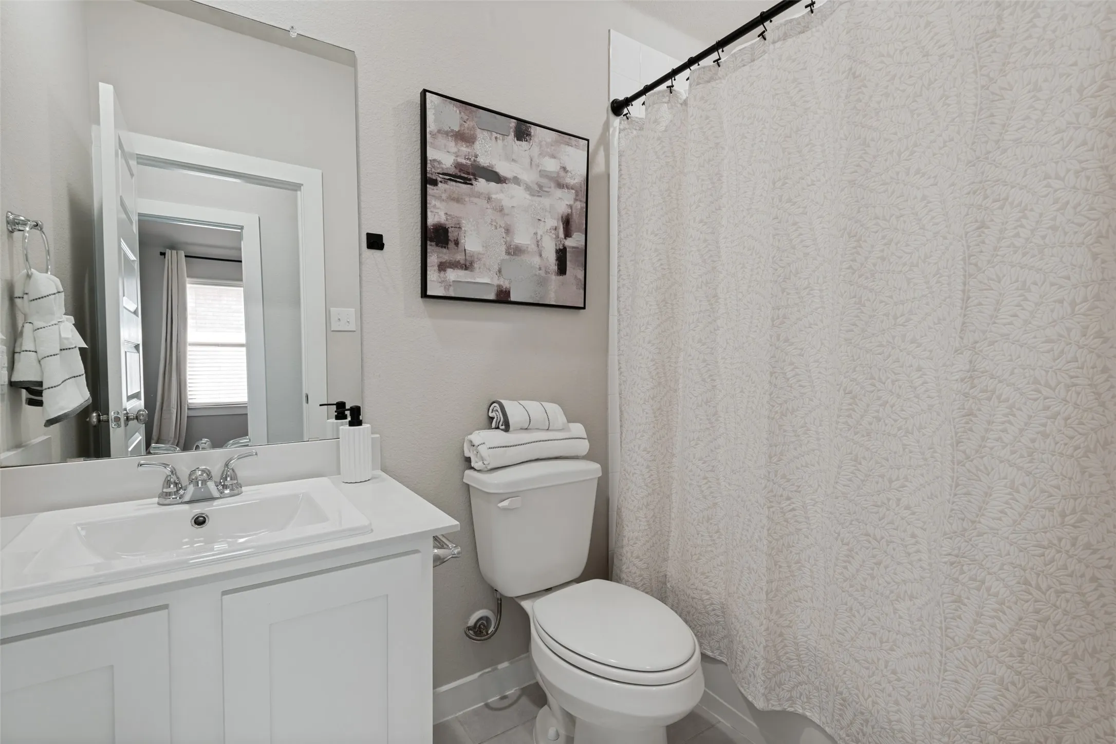 Bathroom featuring a white vanity cabinet with a rectangular basin, chrome dual-handle faucet, integrated countertop, and an expansive wall-mounted mirror