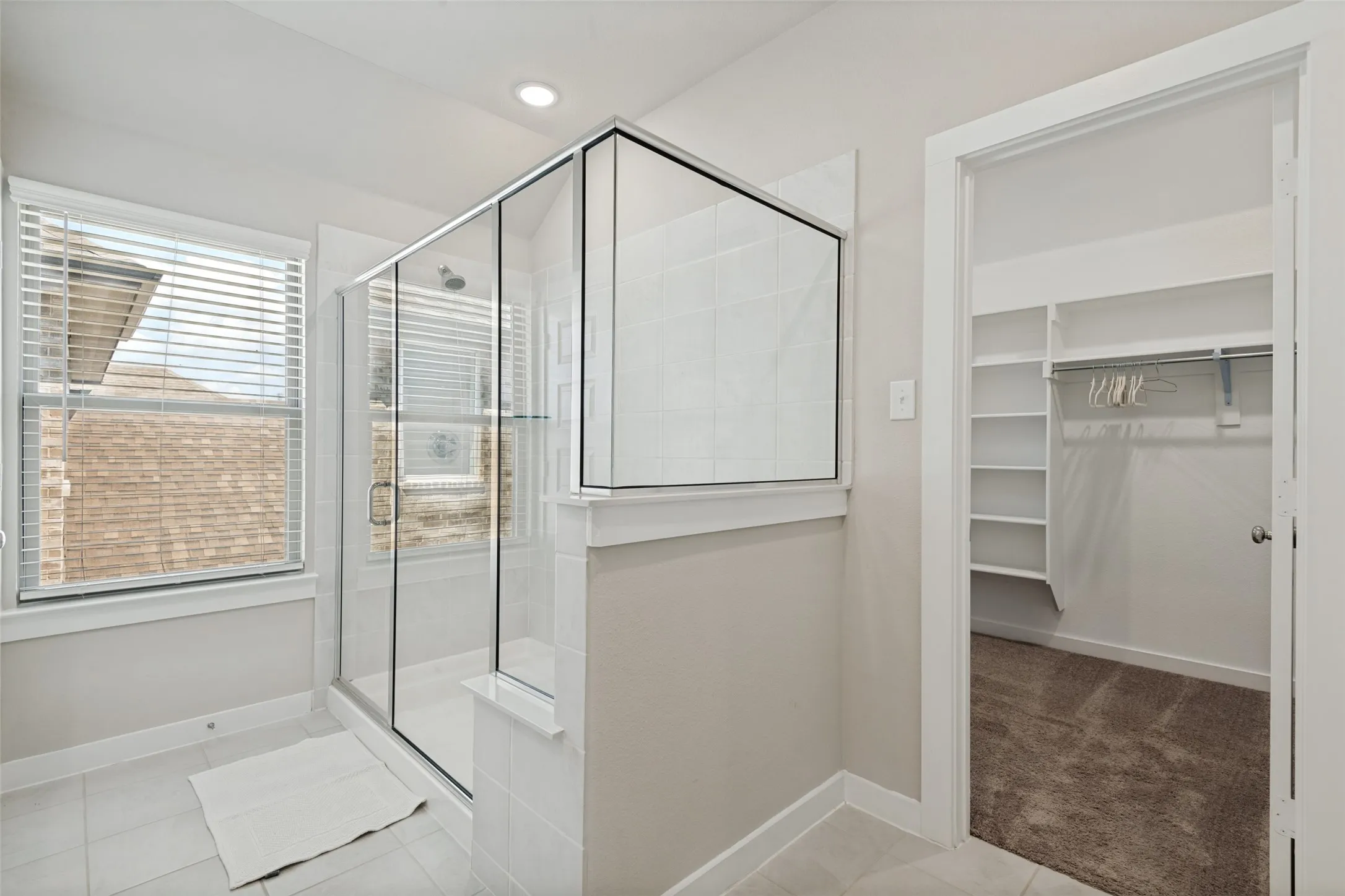Walk-in shower with a glass enclosure, tile surround, recessed lighting, and a walk-in closet featuring built-in shelving