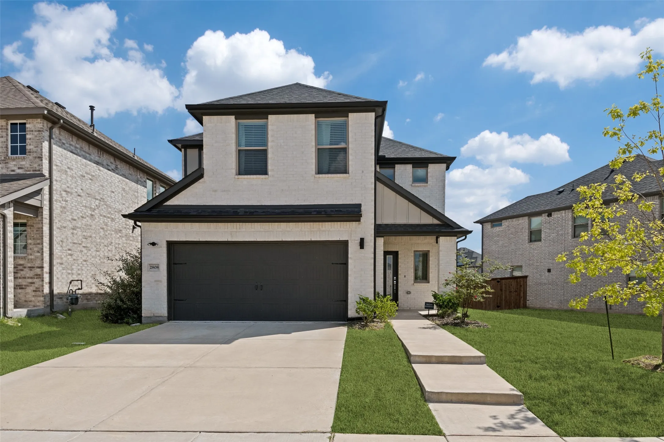 Two-story residence featuring a light-toned brick facade, dark-finish garage door, concrete driveway, and covered entryway