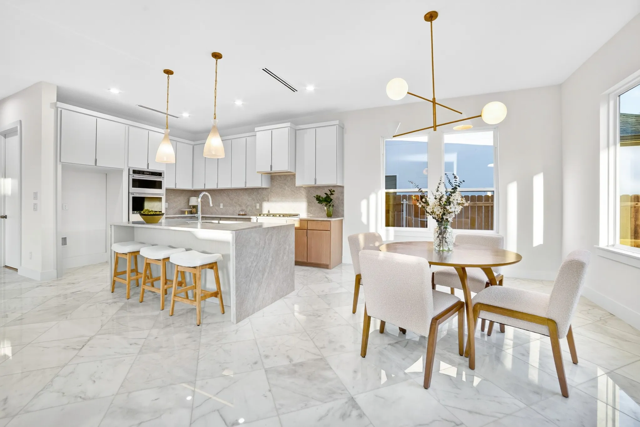 Kitchen featuring stone-topped island with waterfall edge, white cabinetry, integrated stainless steel double wall oven, polished tile flooring, and multi-arm brass light fixture