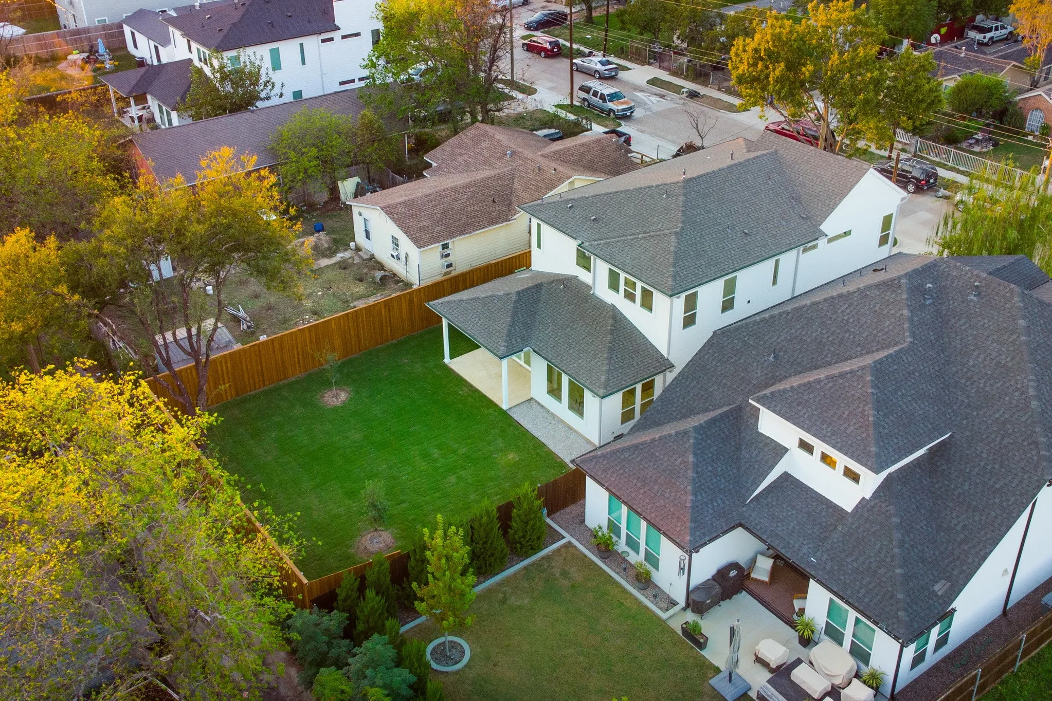 Two-story residence featuring a multi-pitched shingled roof, white exterior siding, a private fenced yard, a covered rear patio, and hardscaped outdoor areas