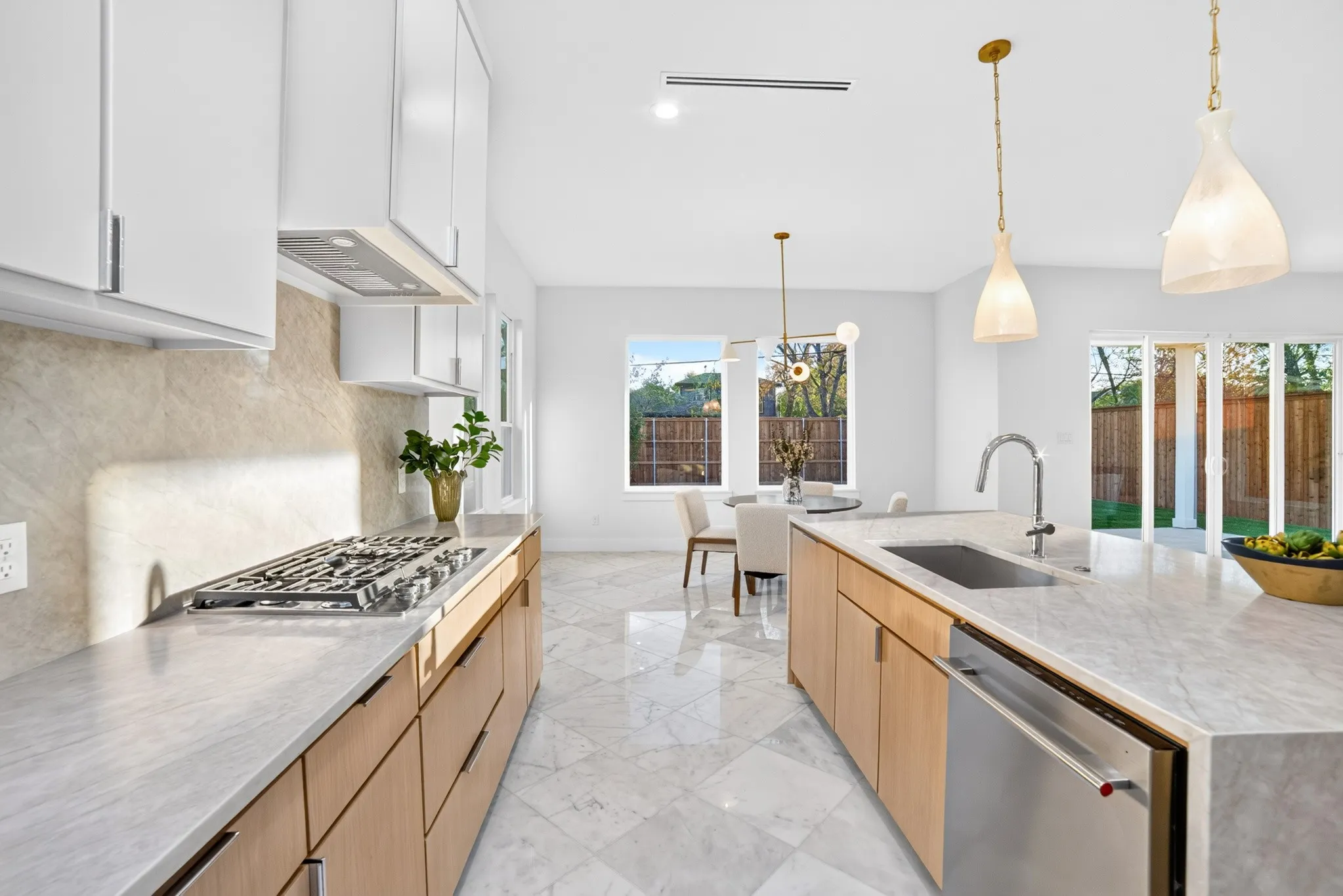 Kitchen featuring light wood-finish cabinetry, stone-patterned countertops with a matching backsplash, a large central island with an integrated sink, polished stone-tile flooring, and glass pendant lighting