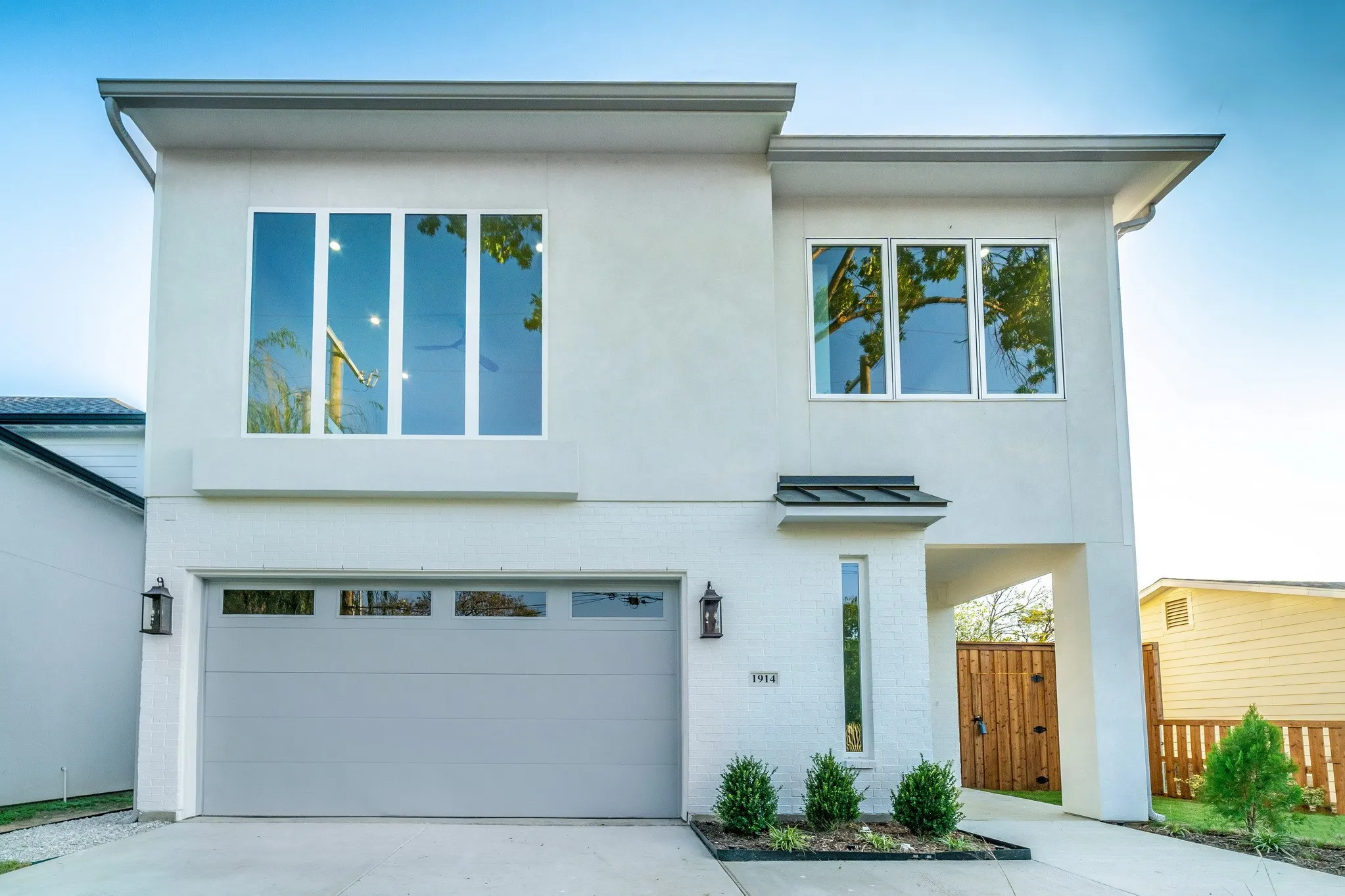 Two-story stucco exterior featuring a flat roofline, oversized multi-pane windows, a dual-car garage, and metal awning accents
