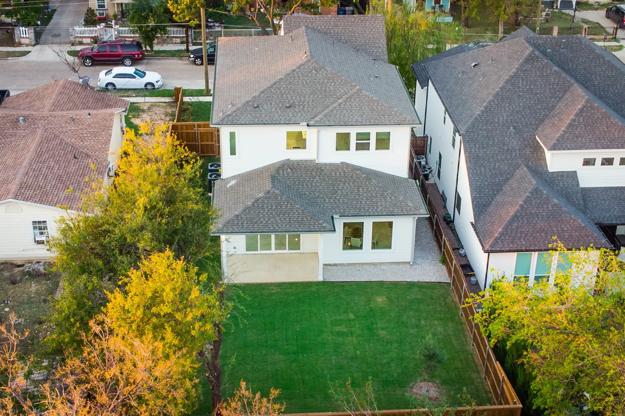 Two-story exterior featuring a light-toned smooth facade, dark asphalt shingle roofing, a ground-level concrete patio, and a fully fenced private rear lawn