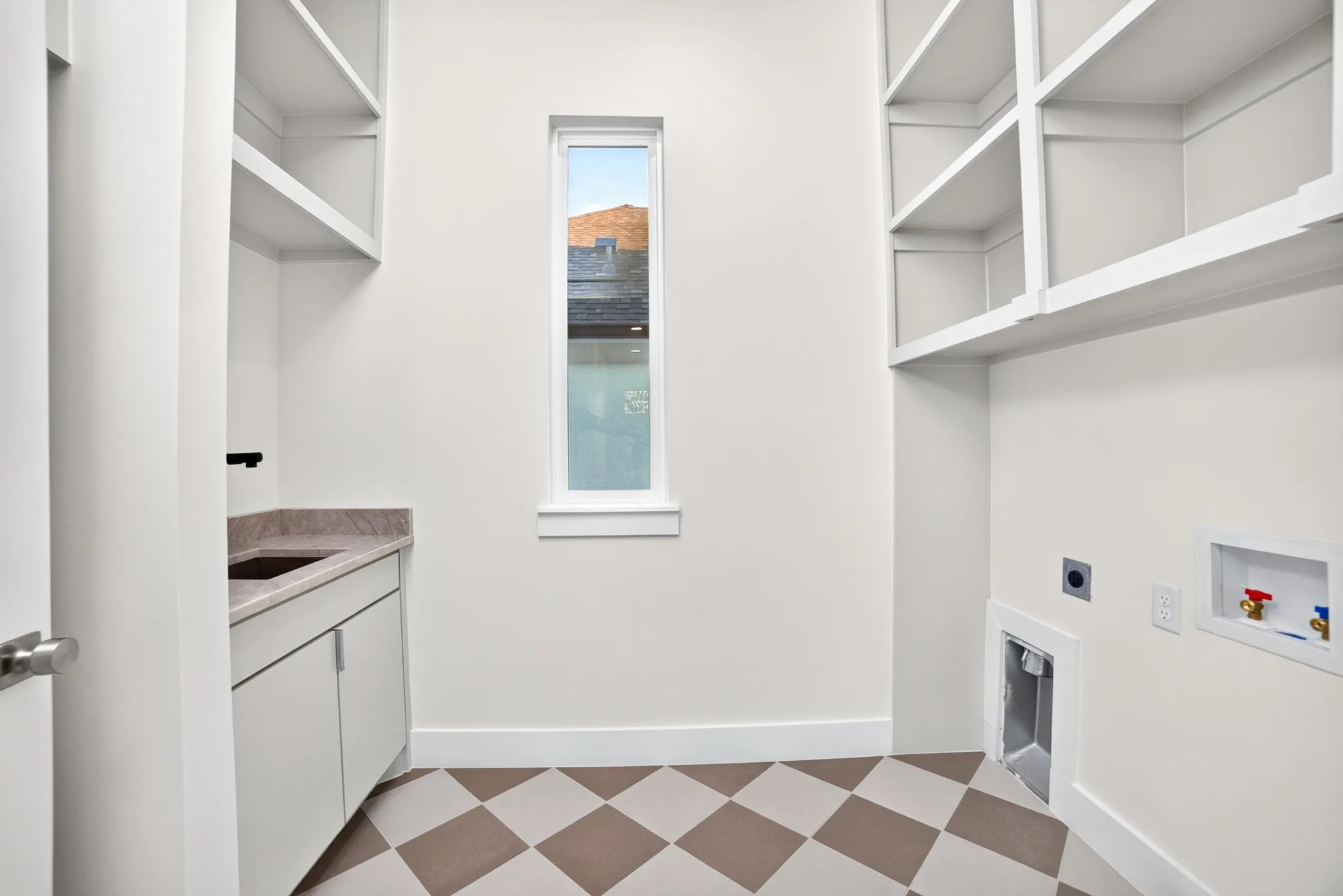 Utility room featuring custom built-in cabinetry, stone-surface countertop with integrated sink, matte black faucet, and checkerboard patterned tile flooring
