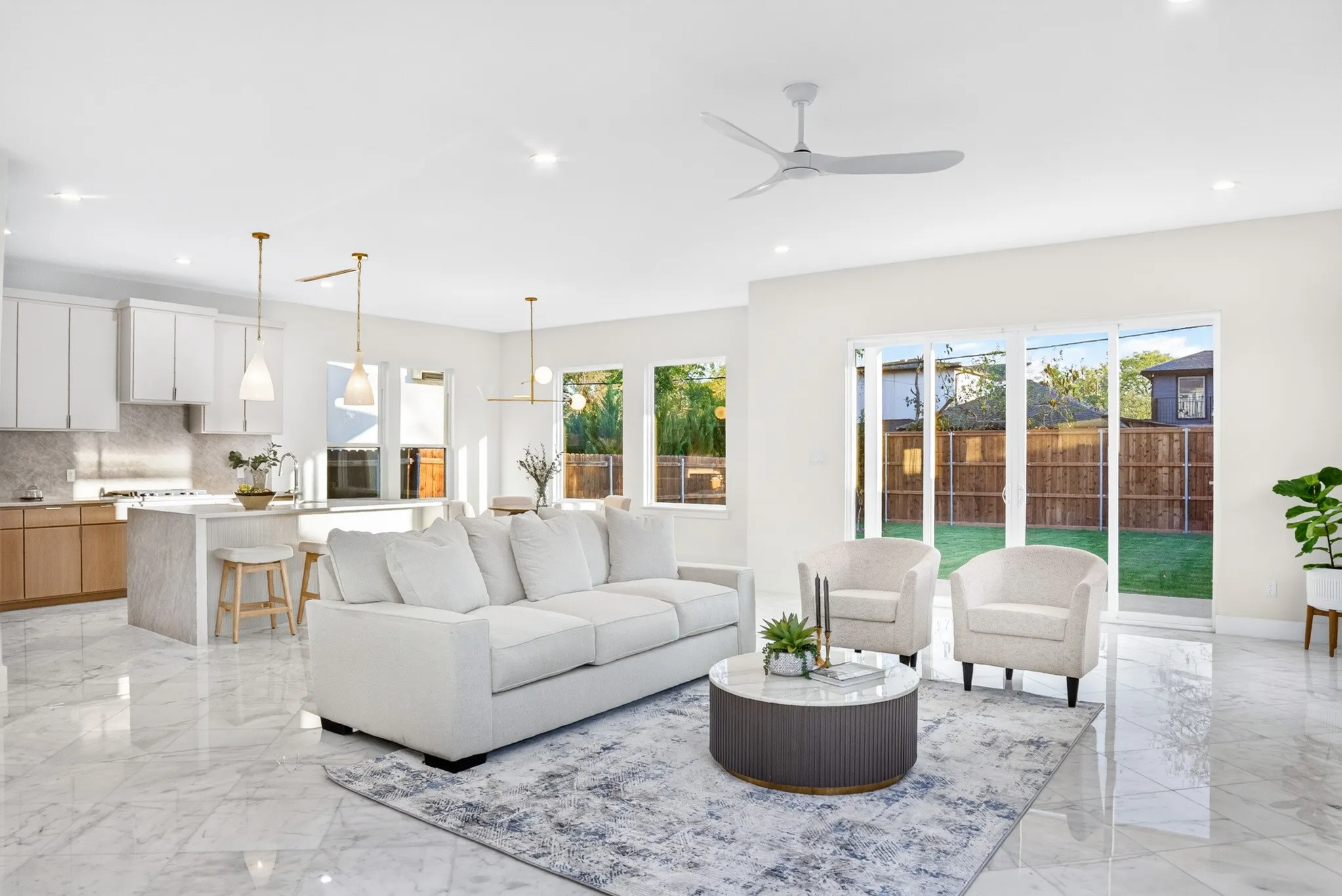 Open-concept interior featuring large-format tile flooring, a central kitchen island with waterfall-edge stone counters, multi-pendant lighting, and floor-to-ceiling sliding glass doors