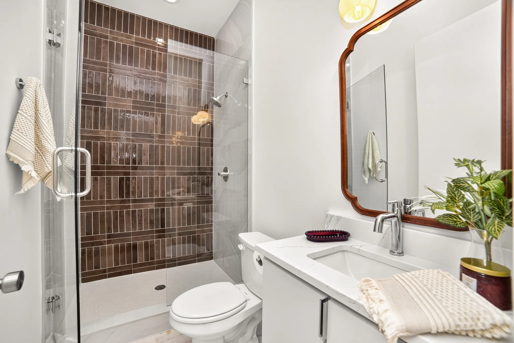 Bathroom featuring a glass-enclosed walk-in shower with vertical tile surround, white vanity with stone-style countertop, integrated sink, and wall-mounted lighting