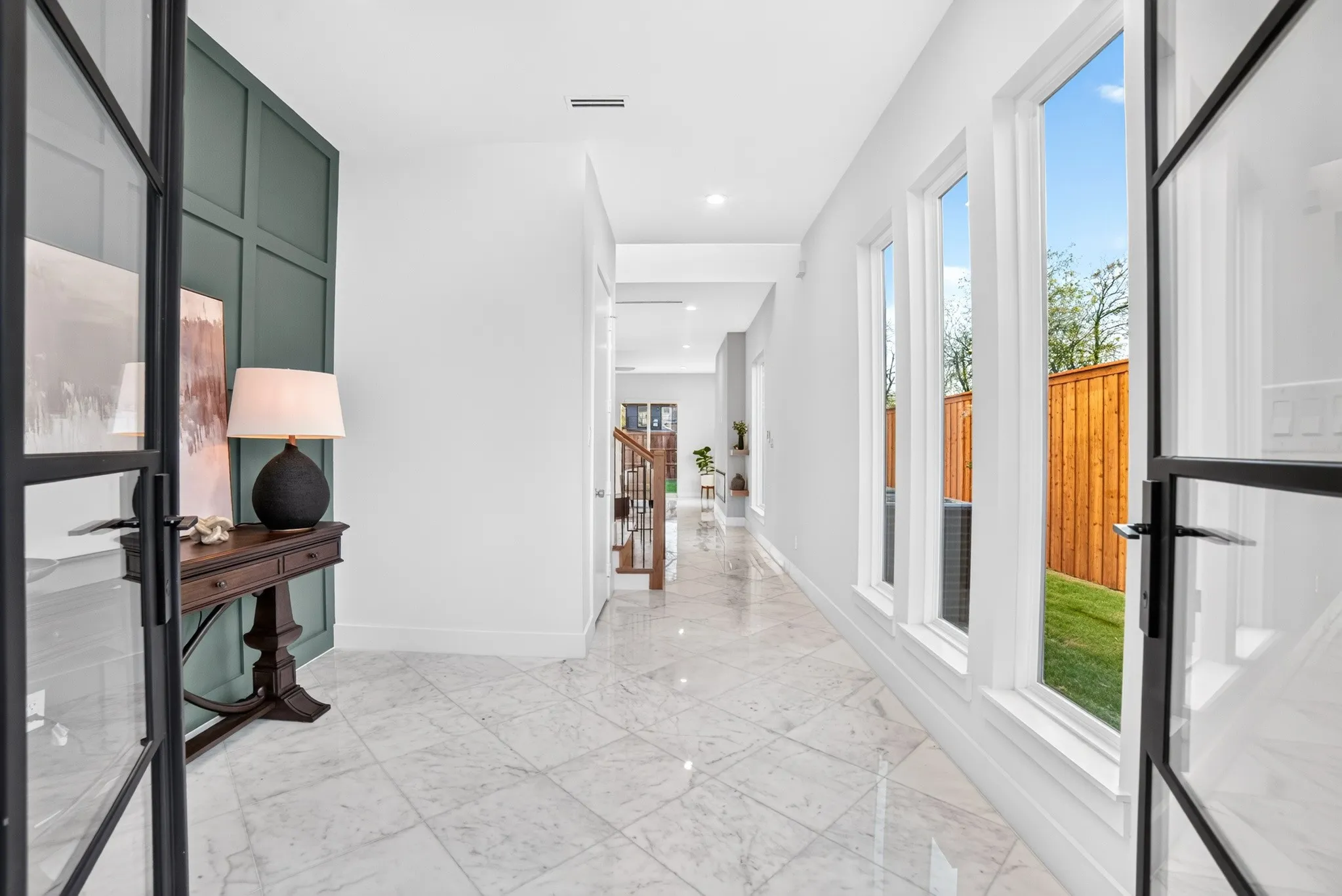 Foyer featuring polished stone flooring, custom green wainscoting, tall windows, and black-trimmed glass French doors