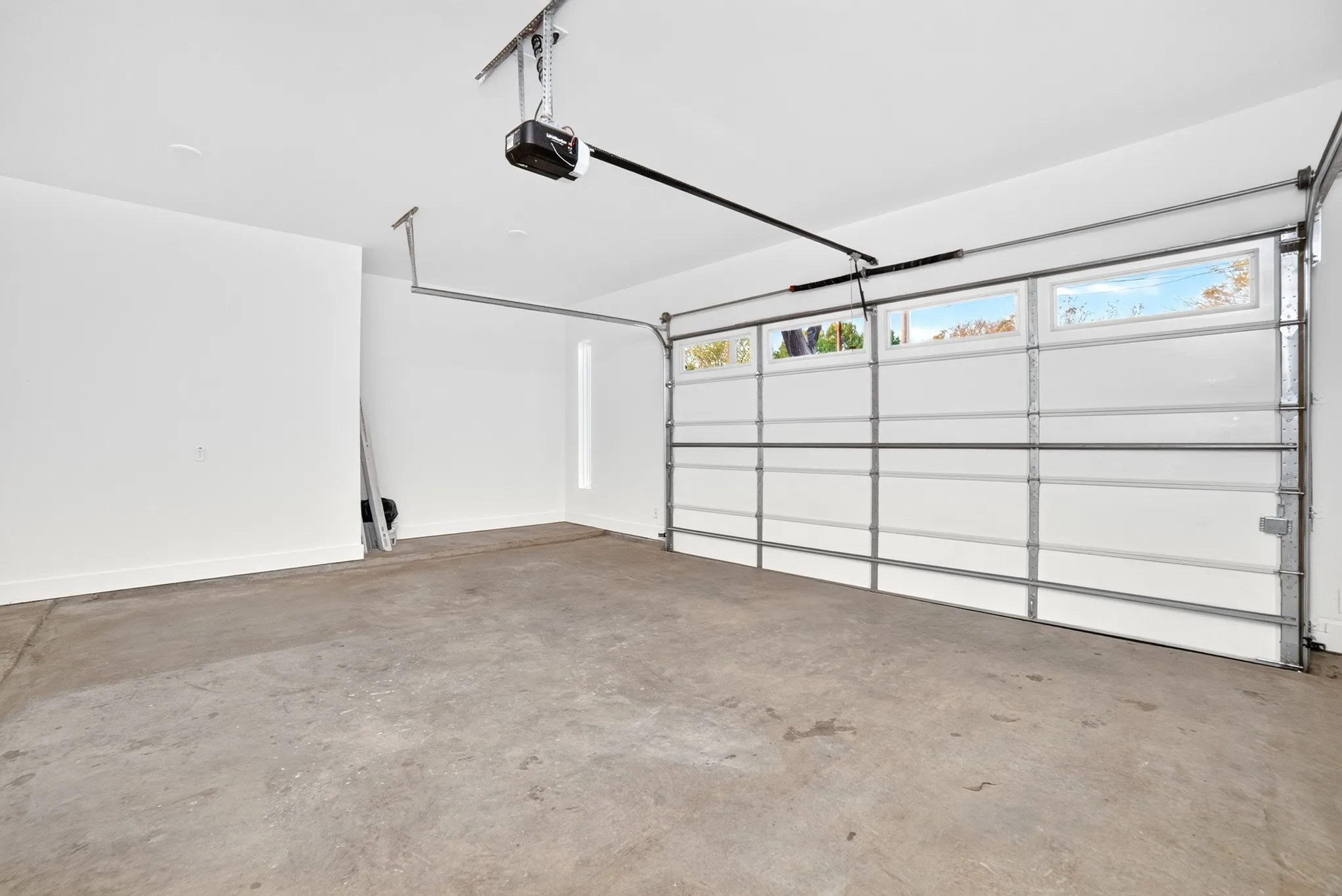 Finished garage featuring concrete flooring, white walls, automated door opener, and a panelled garage door with horizontal glass windows