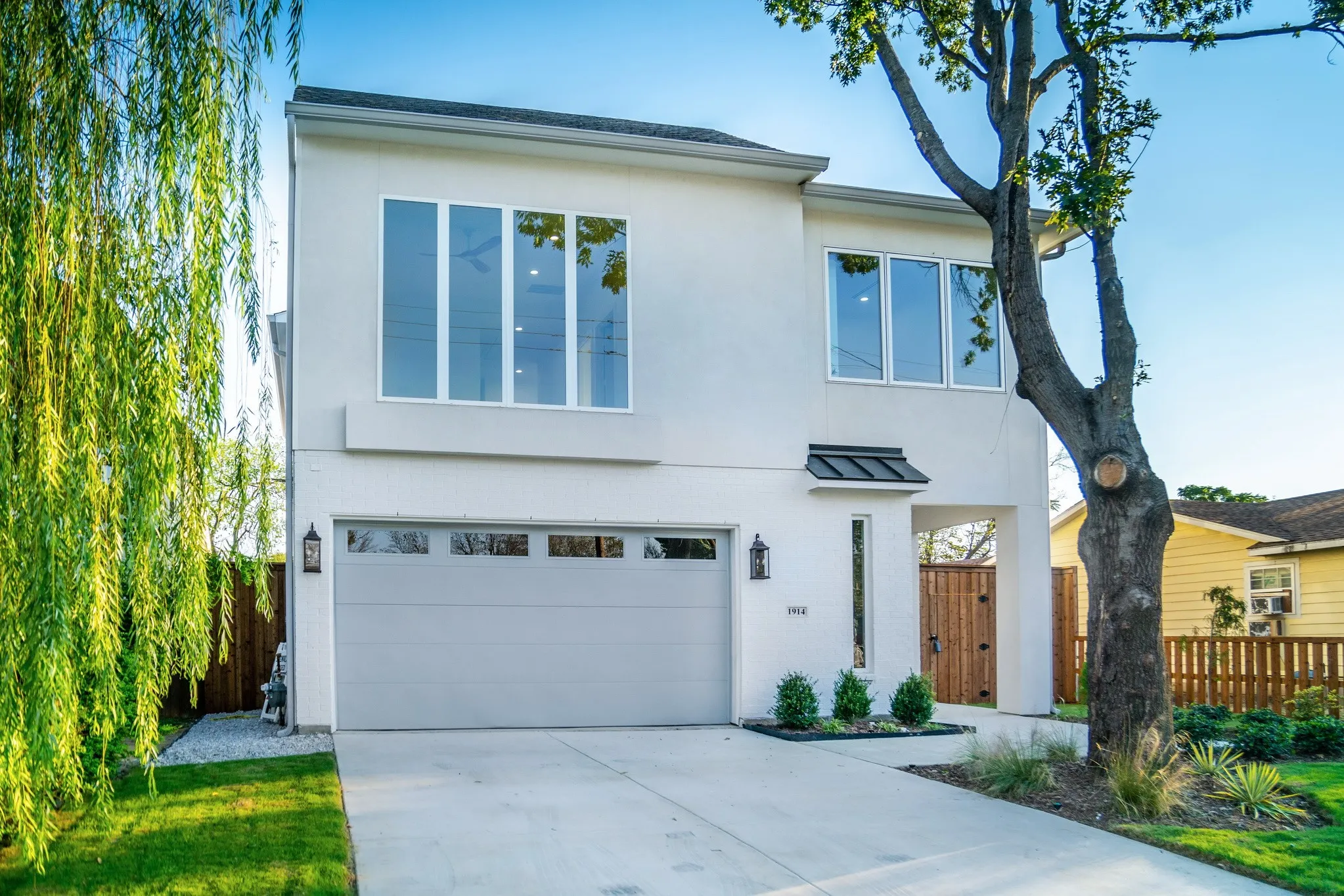Two-story exterior featuring a smooth stucco finish, large-pane windows, a recessed entryway with a metal awning, and a dedicated concrete driveway