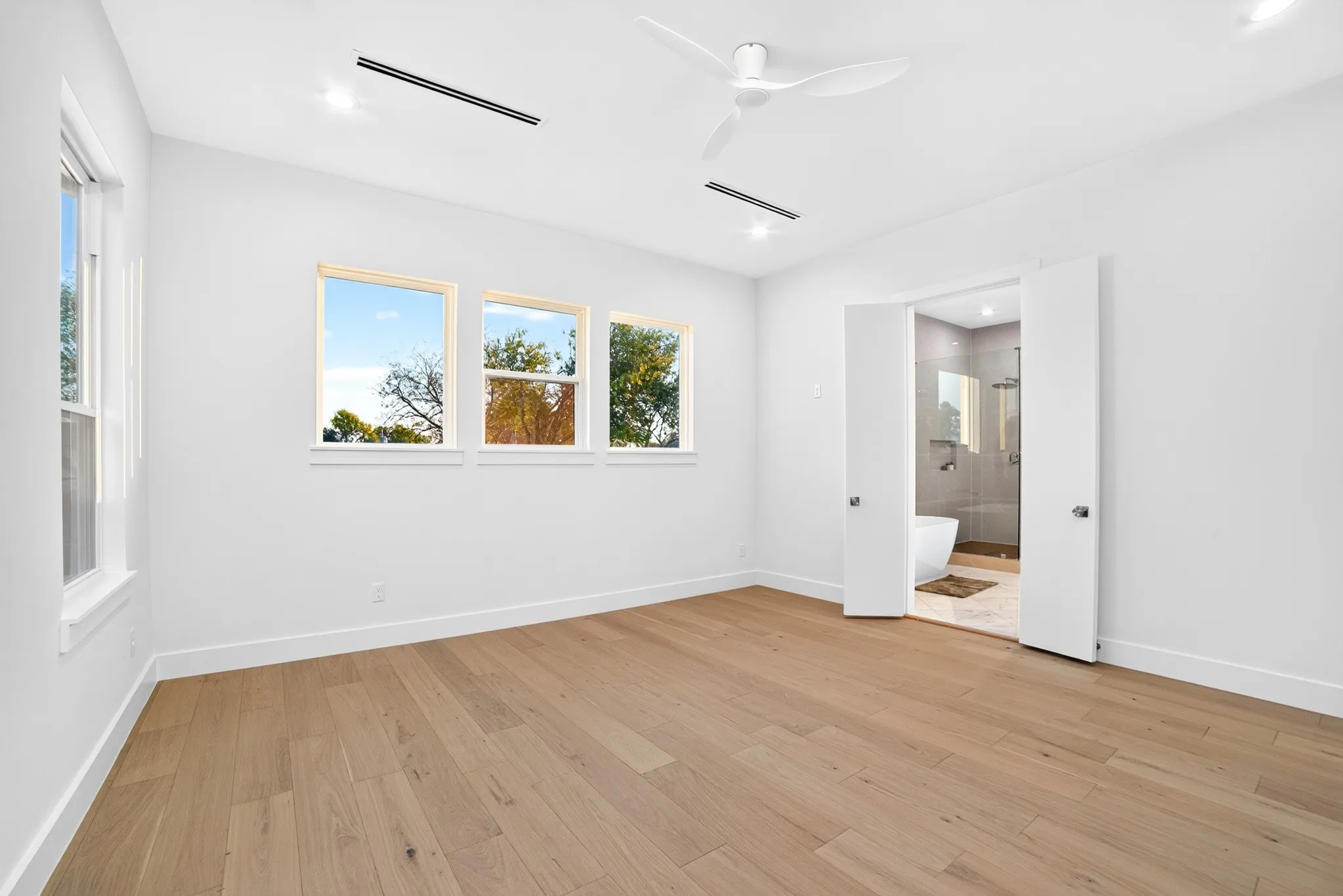 Room featuring wood-finish flooring, recessed lighting, white ceiling fan, and triple-pane window configuration