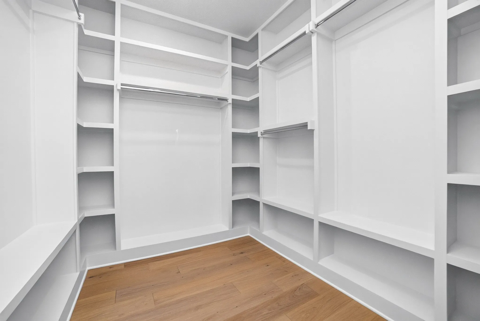 Walk-in closet featuring extensive built-in white shelving, integrated clothing rods, and wood-finish flooring
