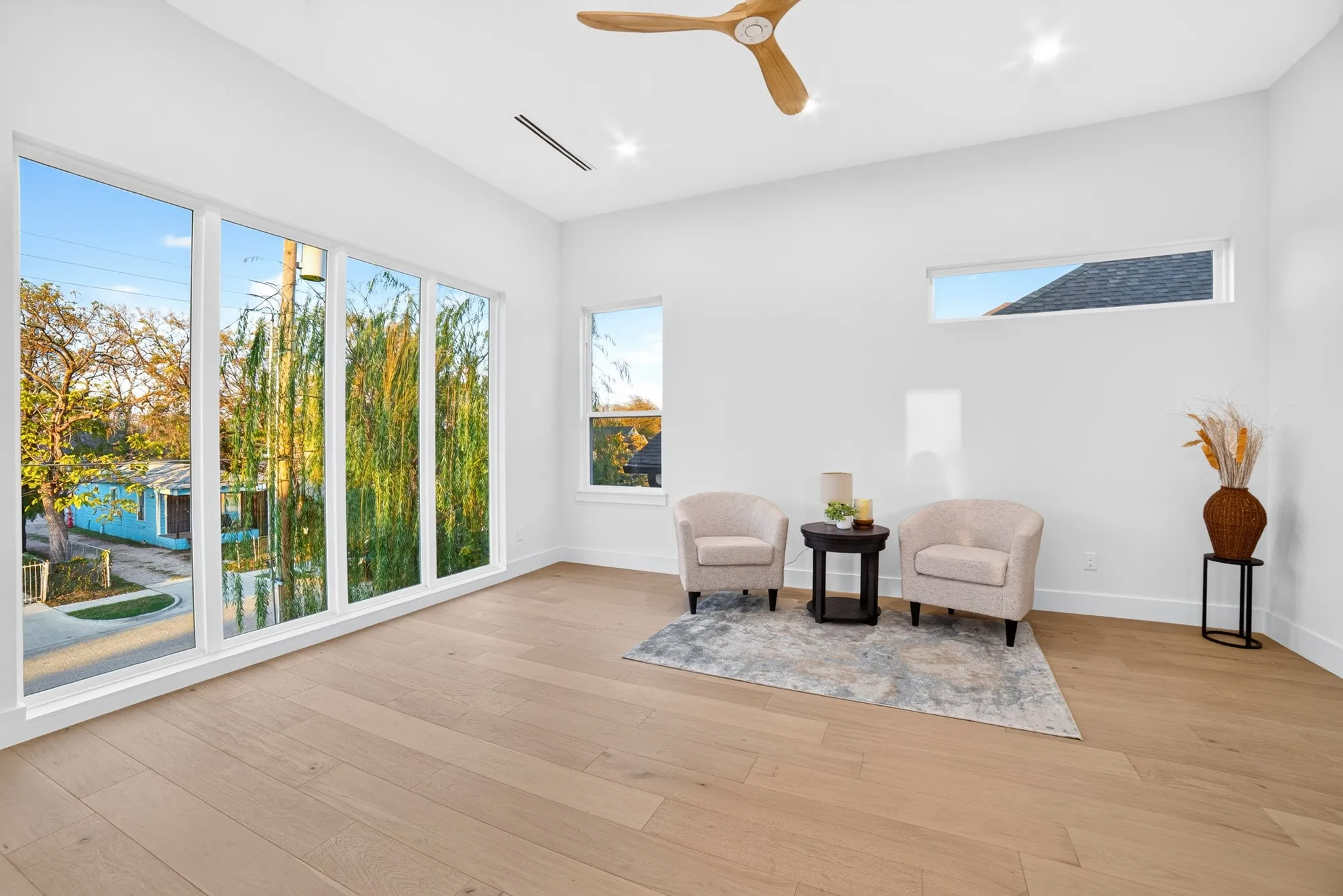 High-ceiling interior featuring light wood-finish flooring, floor-to-ceiling windows, recessed lighting, and a modern wooden ceiling fan