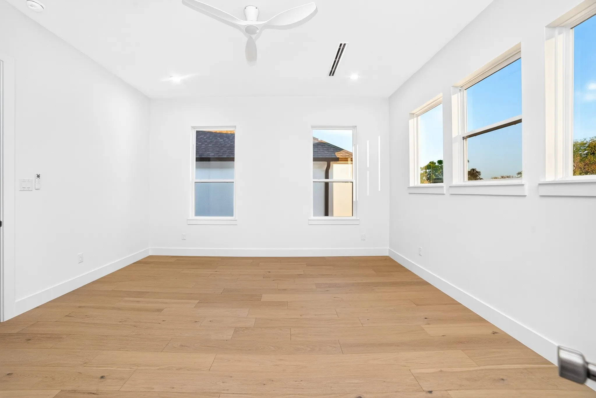 Interior space featuring wood-finish flooring, white walls, multiple windows, a modern white ceiling fan, and recessed lighting