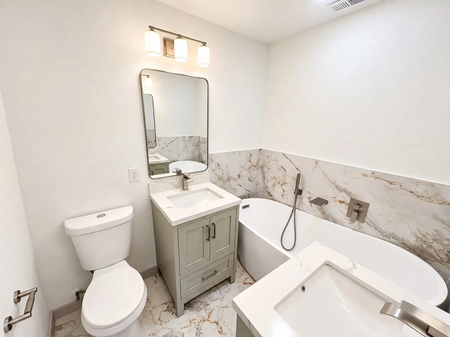 Bathroom featuring a freestanding soaking tub, stone-patterned wall tile, dual vanities with quartz countertops, undermount sinks, and a brushed nickel finish faucet set