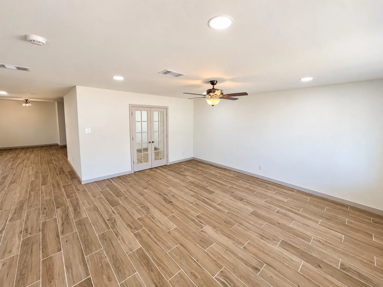 Open interior space featuring wood-finish flooring, recessed lighting, ceiling fans, and French doors