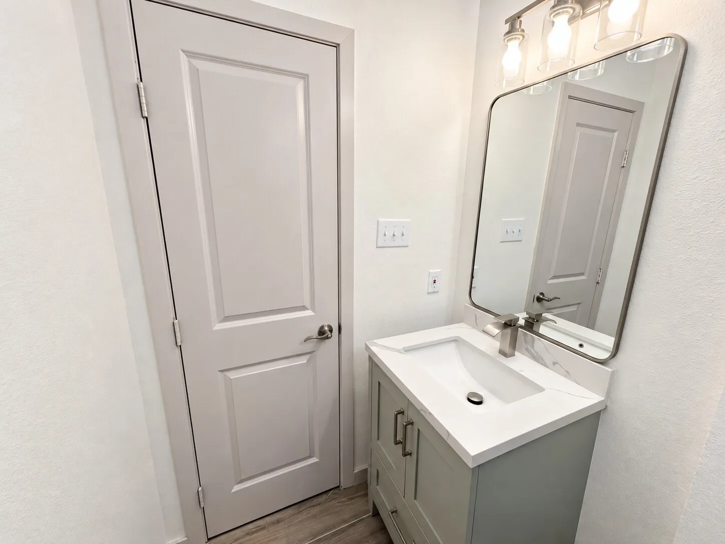 Bathroom featuring a sage green vanity with white stone-finish countertop, integrated rectangular sink, wall-mounted metallic faucet, rounded-corner mirror, and three-light fixture