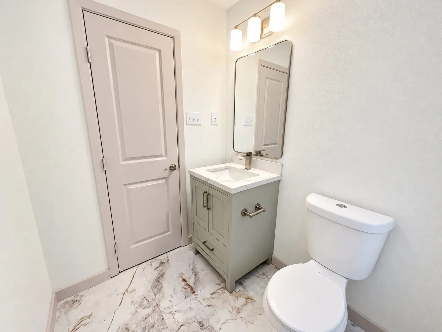 Single-sink vanity with a stone-surface countertop, rectangular undermount basin, rounded-edge wall mirror, three-bulb vanity light, and patterned tile flooring