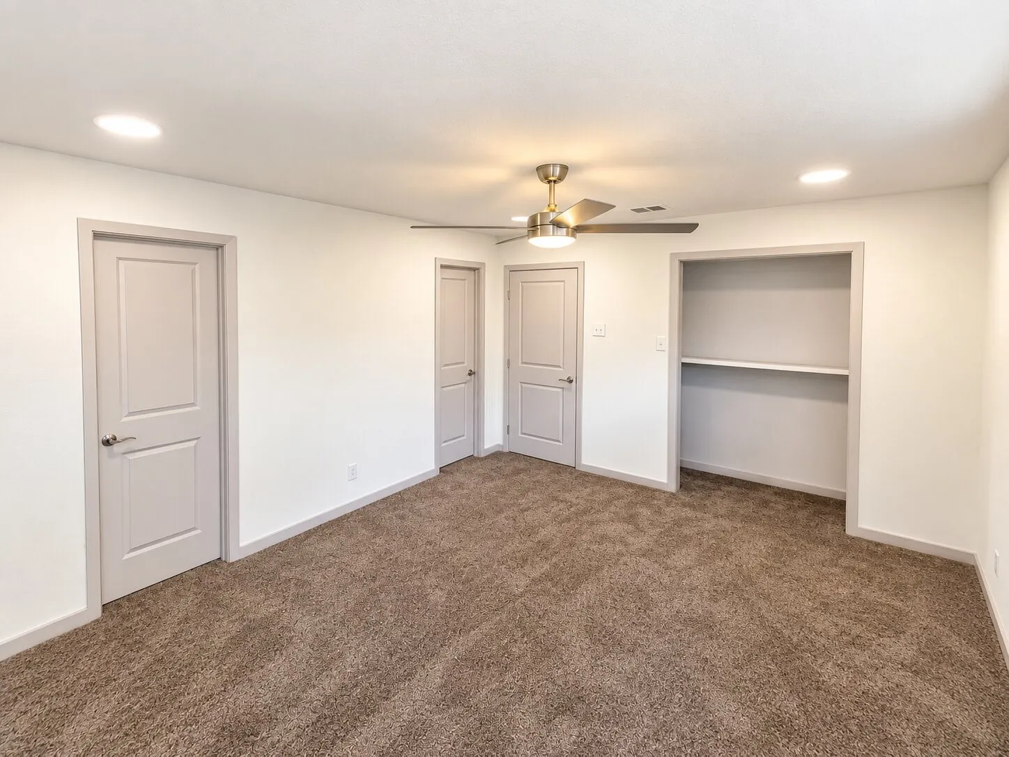 Interior space featuring neutral wall tones, wall-to-wall carpeting, a ceiling-mounted light fixture with fan, recessed lighting, and a built-in closet with shelving