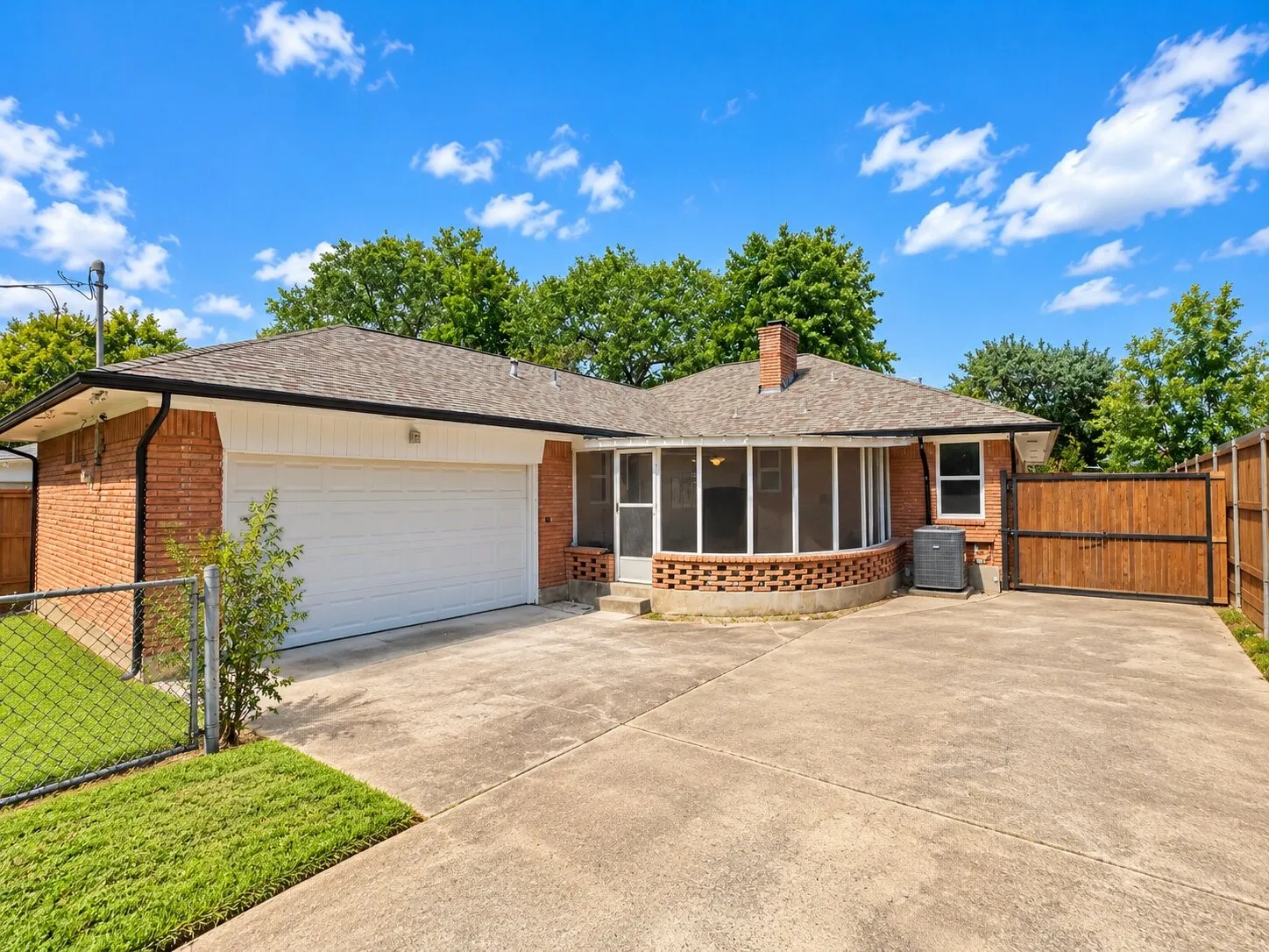 Brick exterior featuring an attached two-car garage, enclosed porch with a masonry base, concrete driveway, and wood privacy fencing