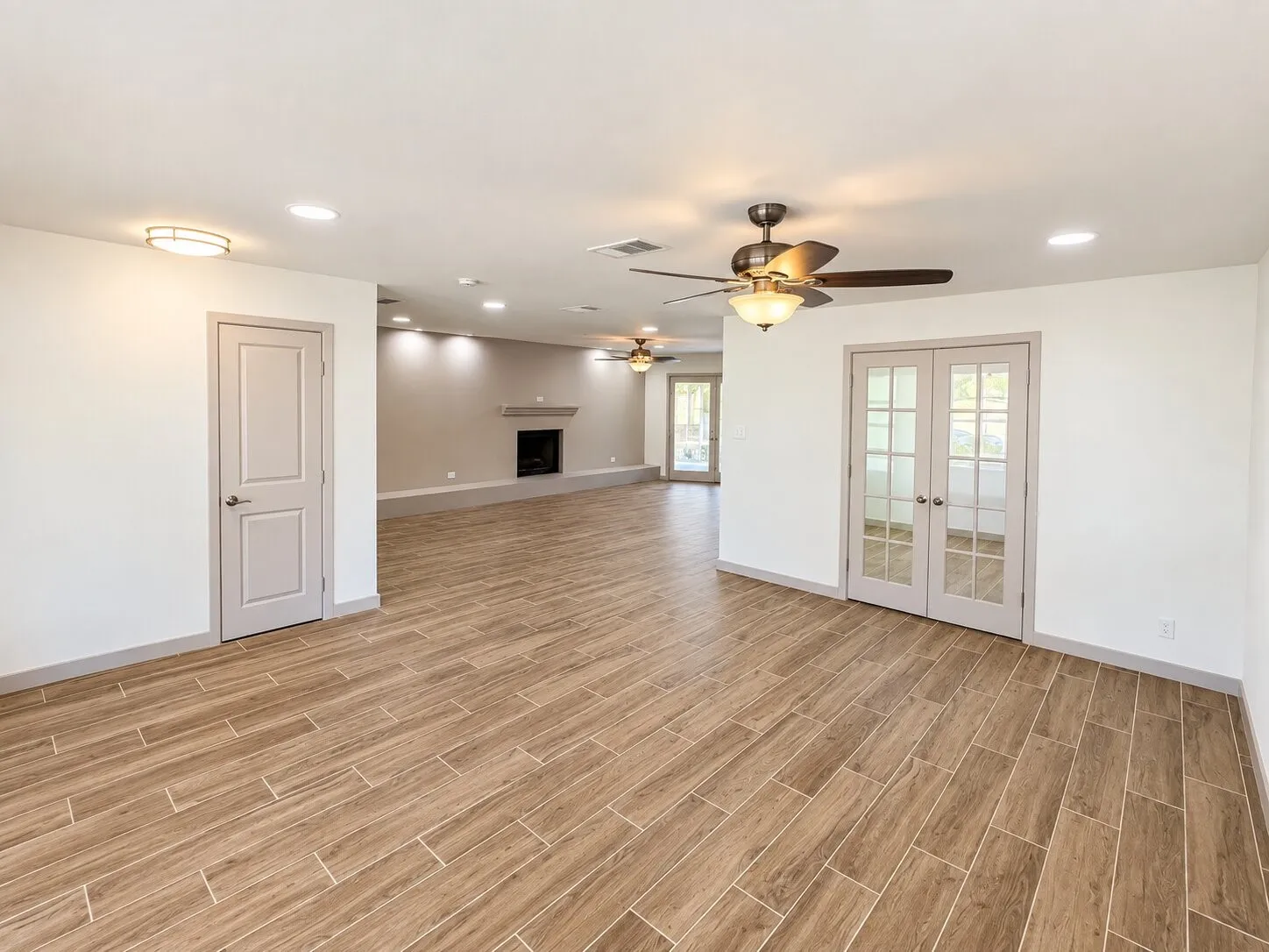 Open-concept interior featuring wood-finish flooring, recessed lighting, ceiling fans, a built-in fireplace with a raised hearth, and double French doors with glass panes