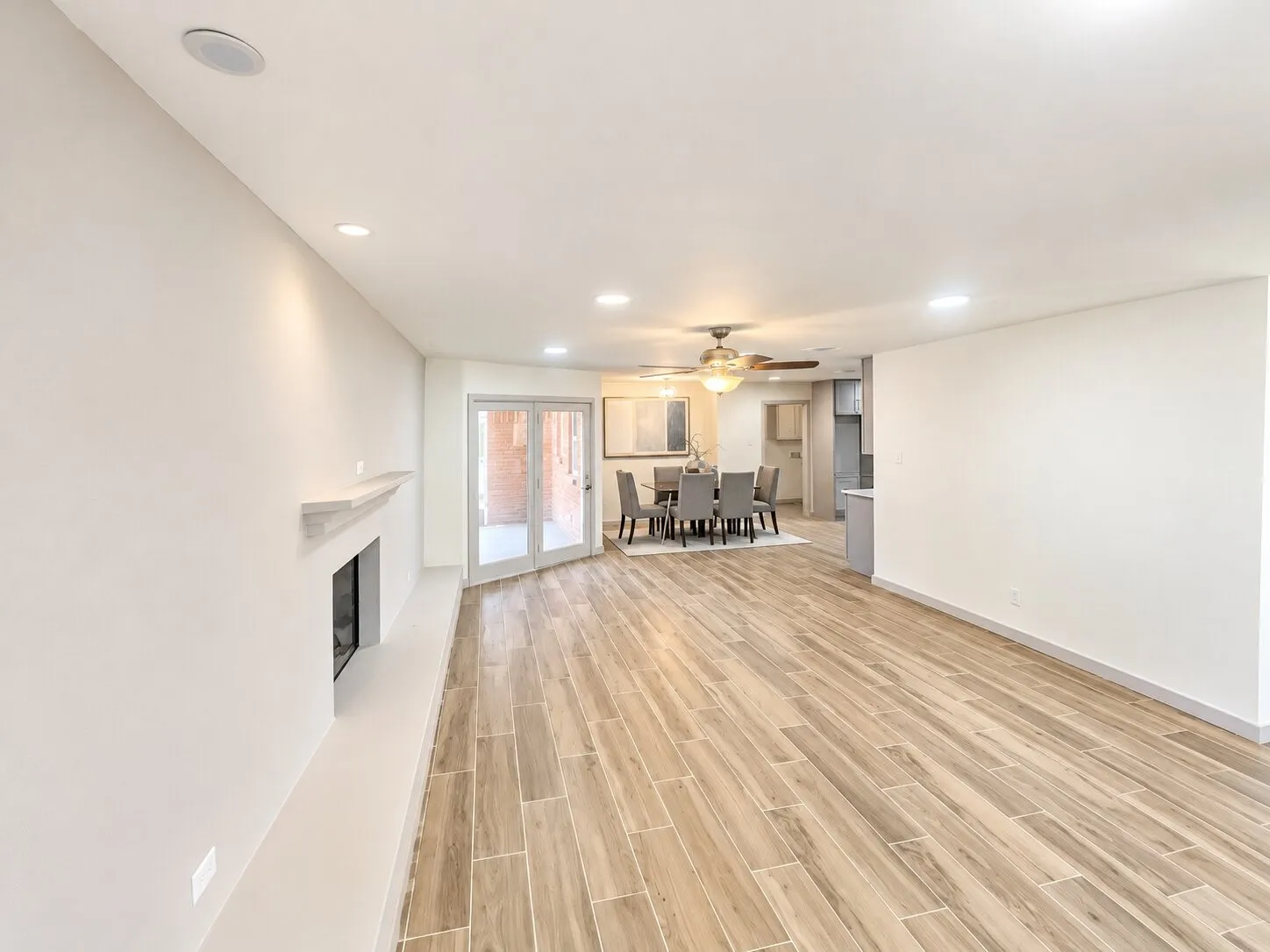 Open floor plan featuring wood-finish flooring, recessed lighting, a fireplace with a mantel, and double doors opening to an exterior area