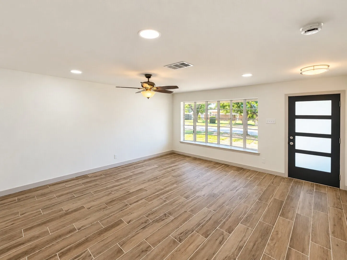 Wood-finish flooring, recessed lighting, ceiling fan with light kit, expansive window with grid panes, and a modern entry door featuring four frosted glass panels