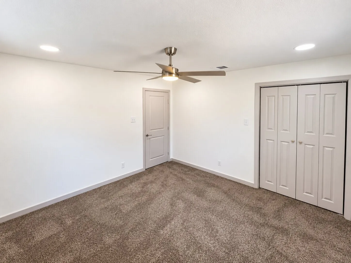 Neutral-toned carpeting, recessed ceiling lighting, a brushed-nickel ceiling fan, and paneled closet doors