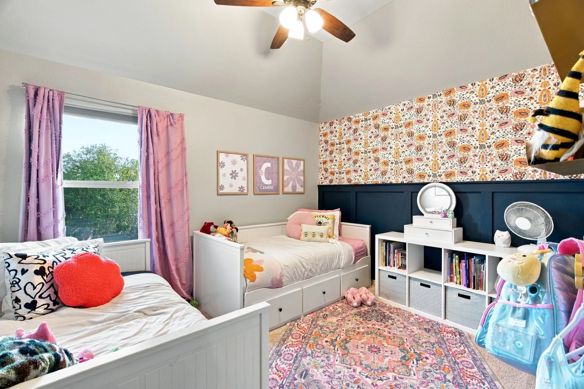 Vaulted ceiling featuring a central ceiling fan with an integrated light fixture, dark-toned wainscoting, and patterned wallpaper