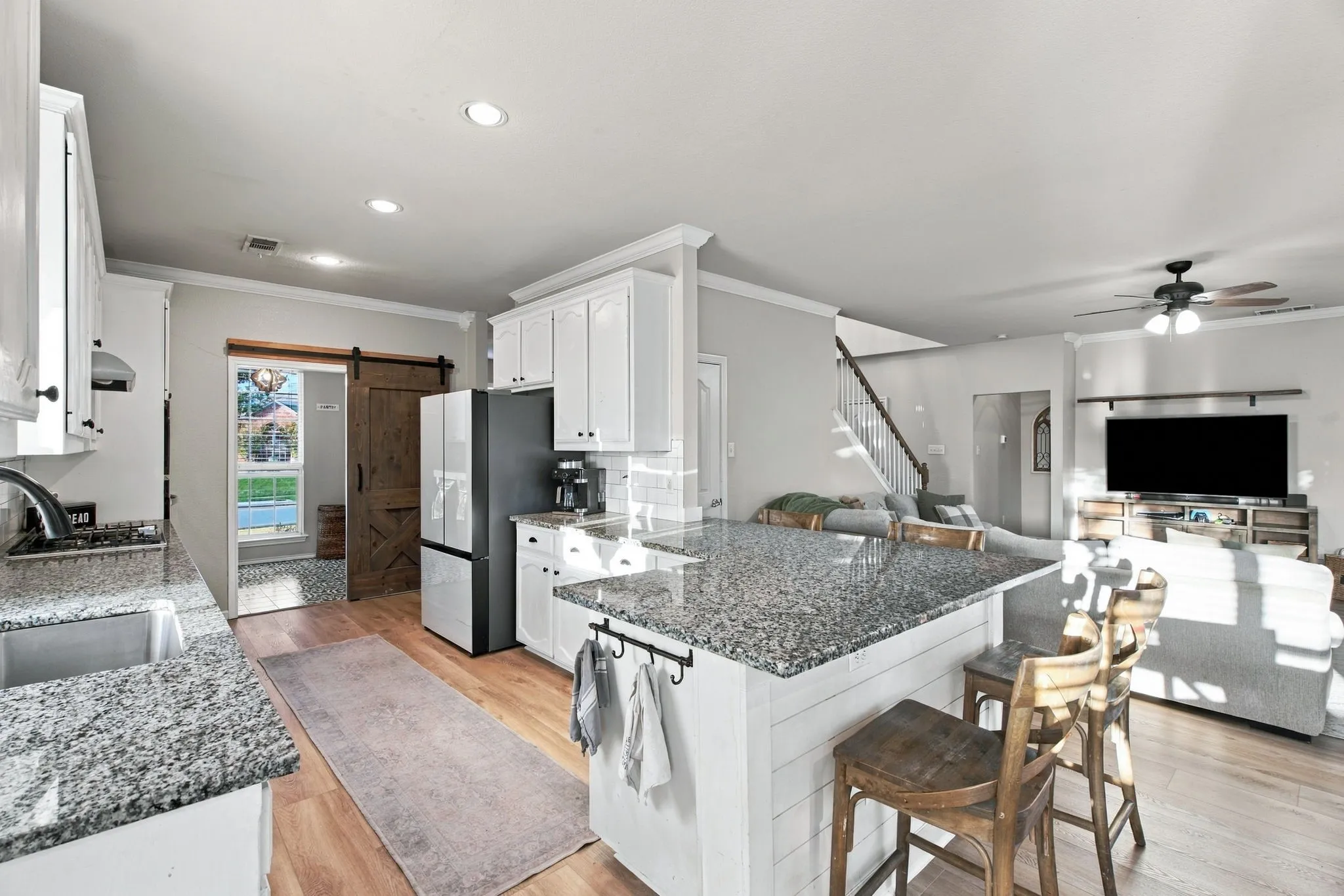 Kitchen featuring white cabinetry, stone countertops, an island with shiplap detailing, wood-finish flooring, and a sliding barn door
