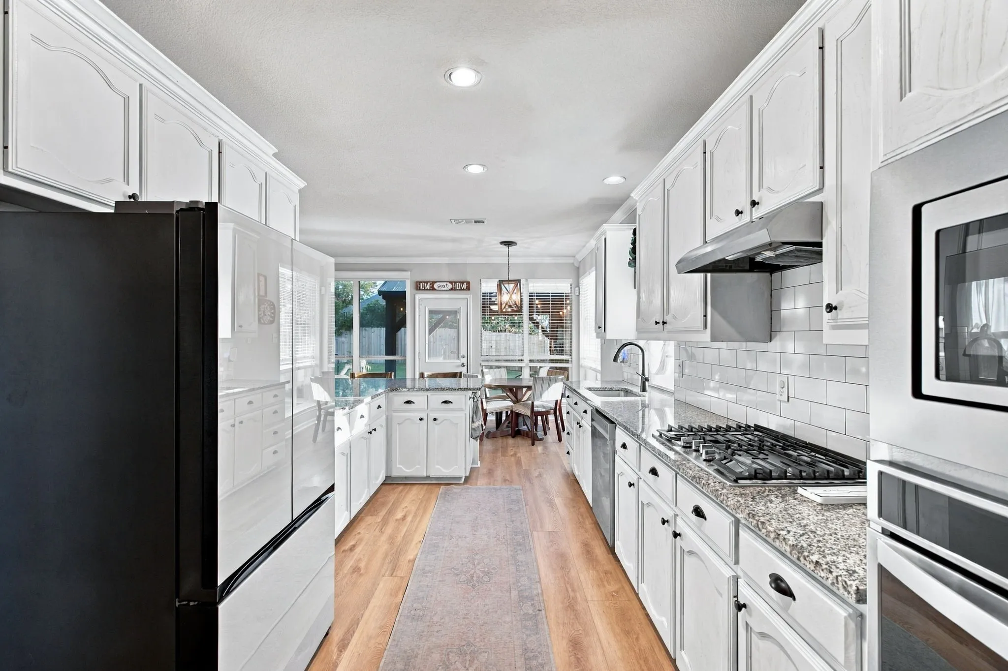 Kitchen featuring white cabinetry, stone countertops, subway tile backsplash, stainless steel appliances, and wood-finish flooring