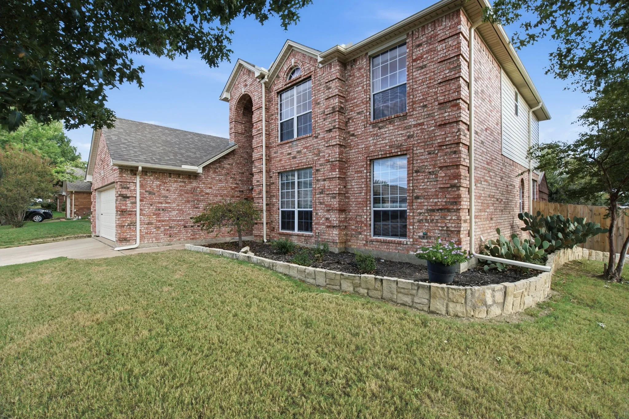 Two-story brick exterior featuring a multi-gabled roofline, grid-pattern windows, attached garage, and stone-bordered landscaping