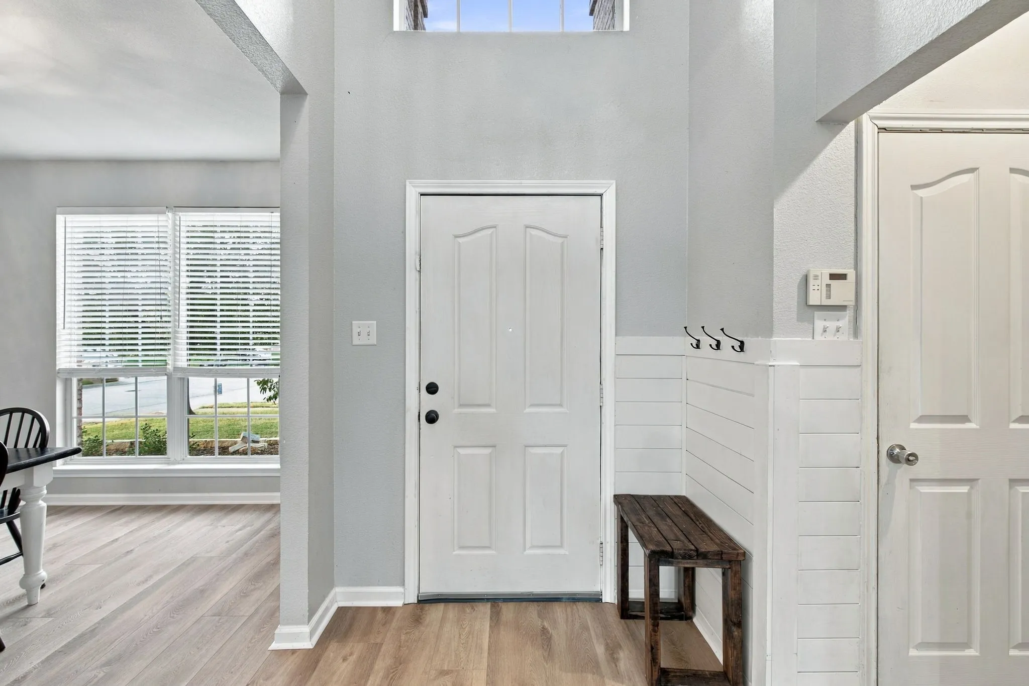 Entryway featuring high ceilings, a transom window, wood-finish flooring, and white shiplap wainscoting with integrated wall-mounted hooks