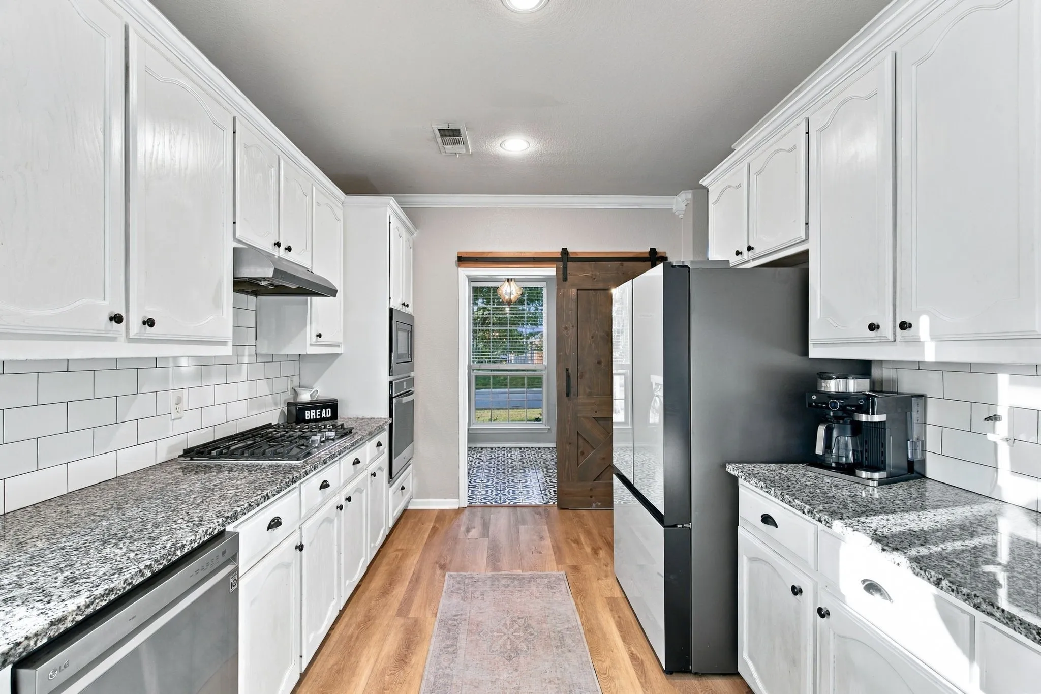 Kitchen featuring white cabinetry, stone countertops, subway tile backsplash, stainless steel appliances, and wood-finish flooring