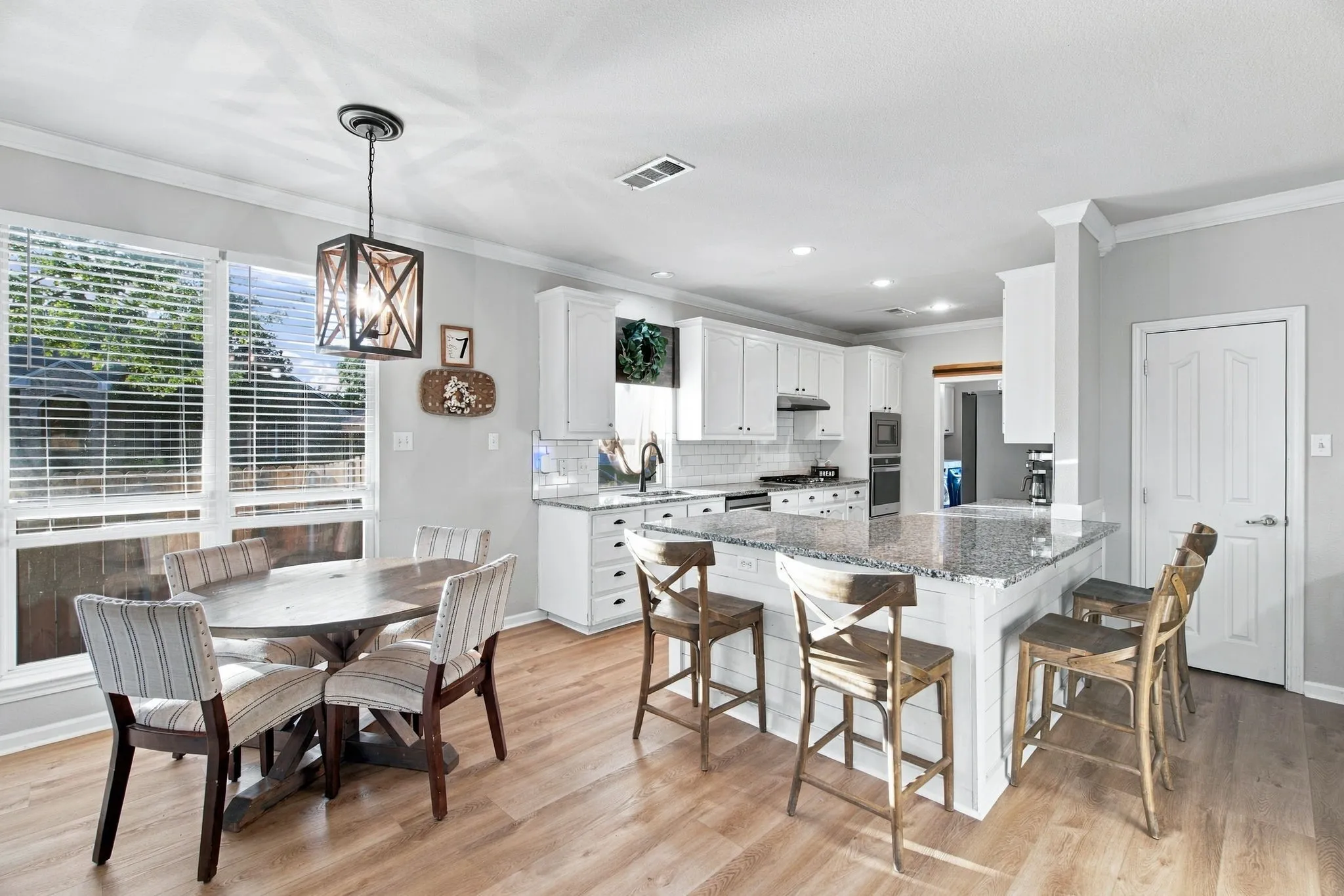 Kitchen featuring white shaker-style cabinetry, stone countertops, a center island with shiplap detailing, wood-finish flooring, and a geometric pendant light fixture