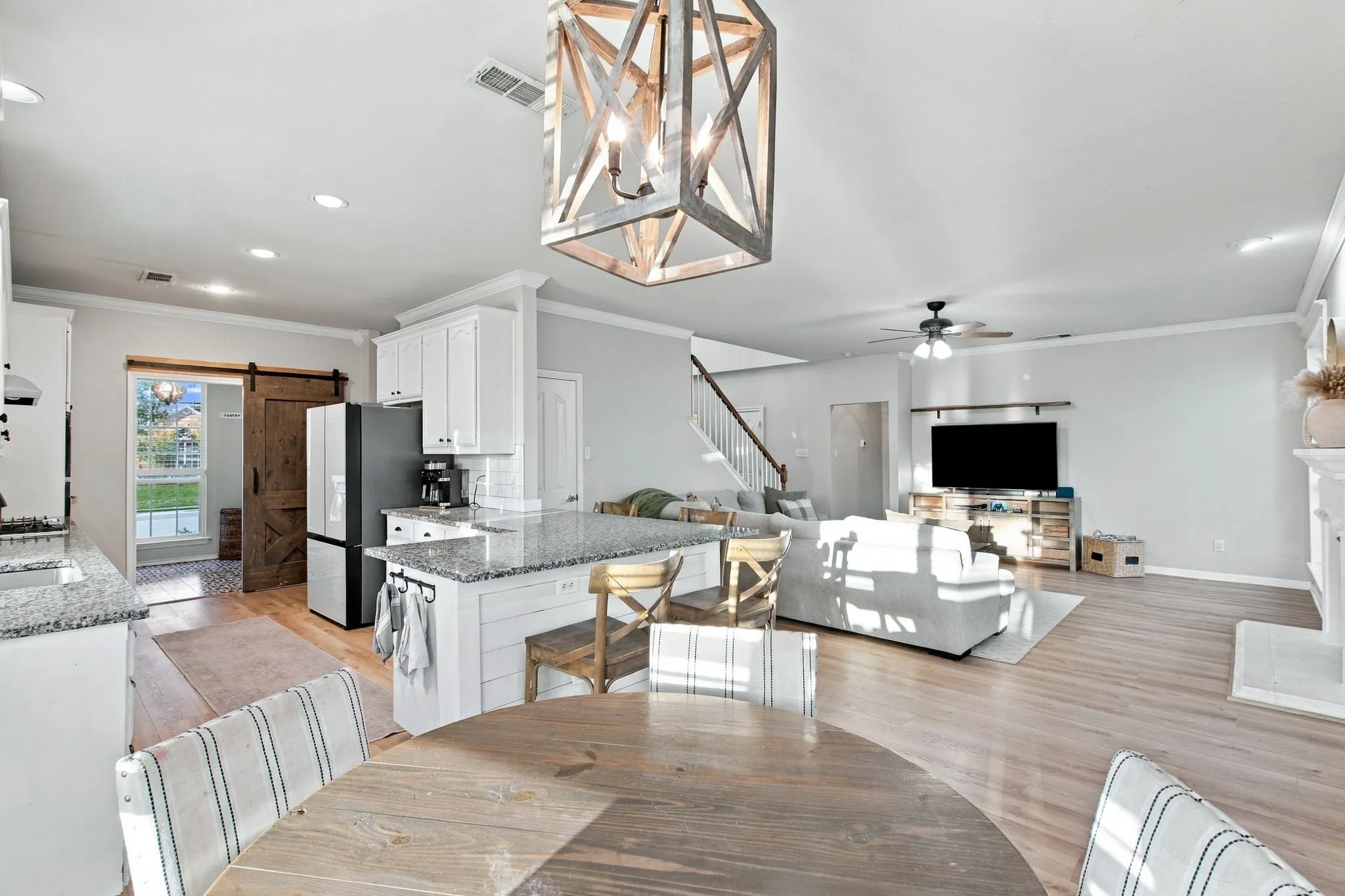 Open concept area featuring light wood-finish flooring, a kitchen island with stone countertops, a geometric chandelier, and a sliding barn door