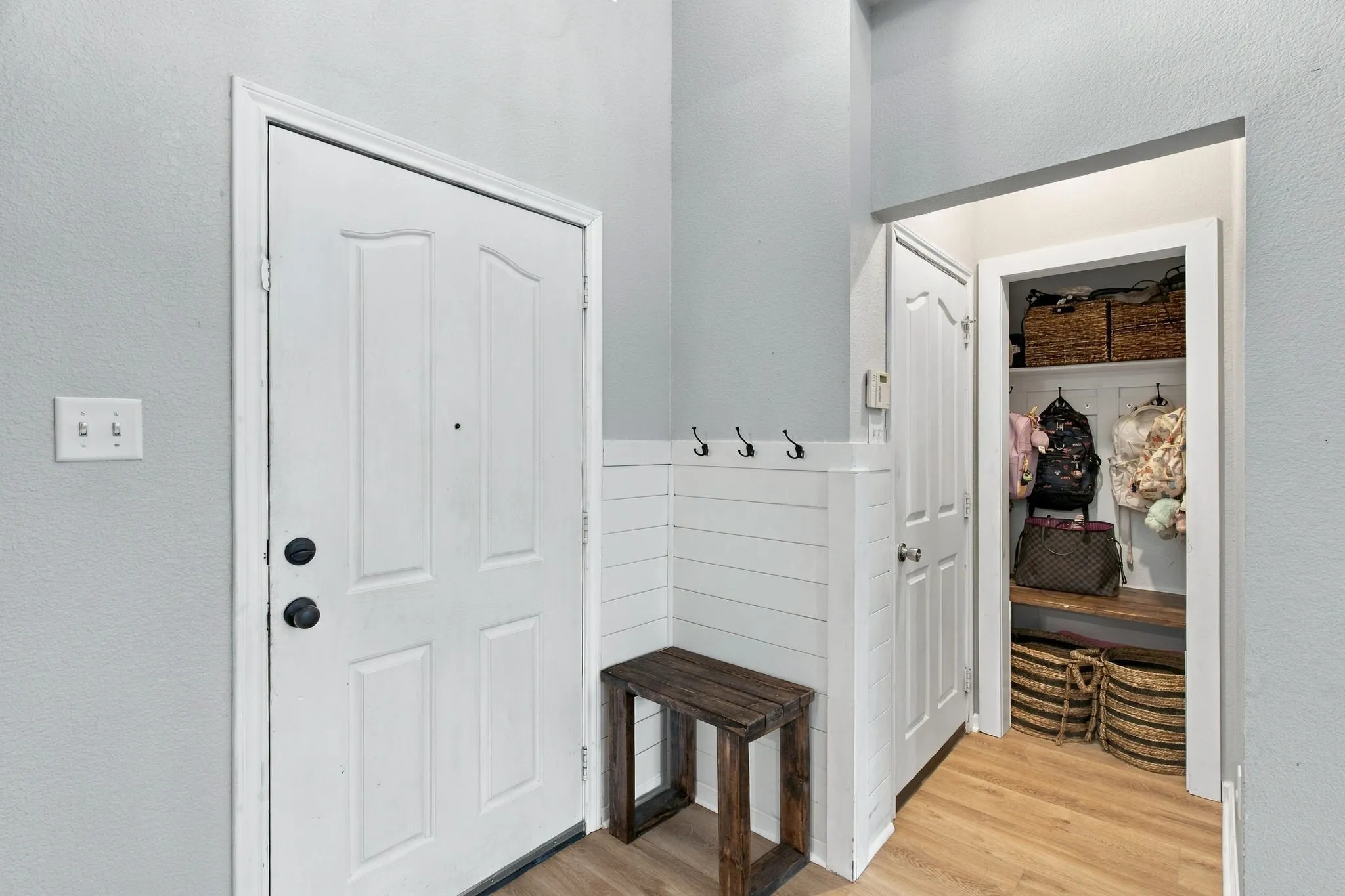 Entryway featuring white shiplap wainscoting with integrated wall hooks, wood-finish flooring, and a walk-in storage area with built-in wooden shelving