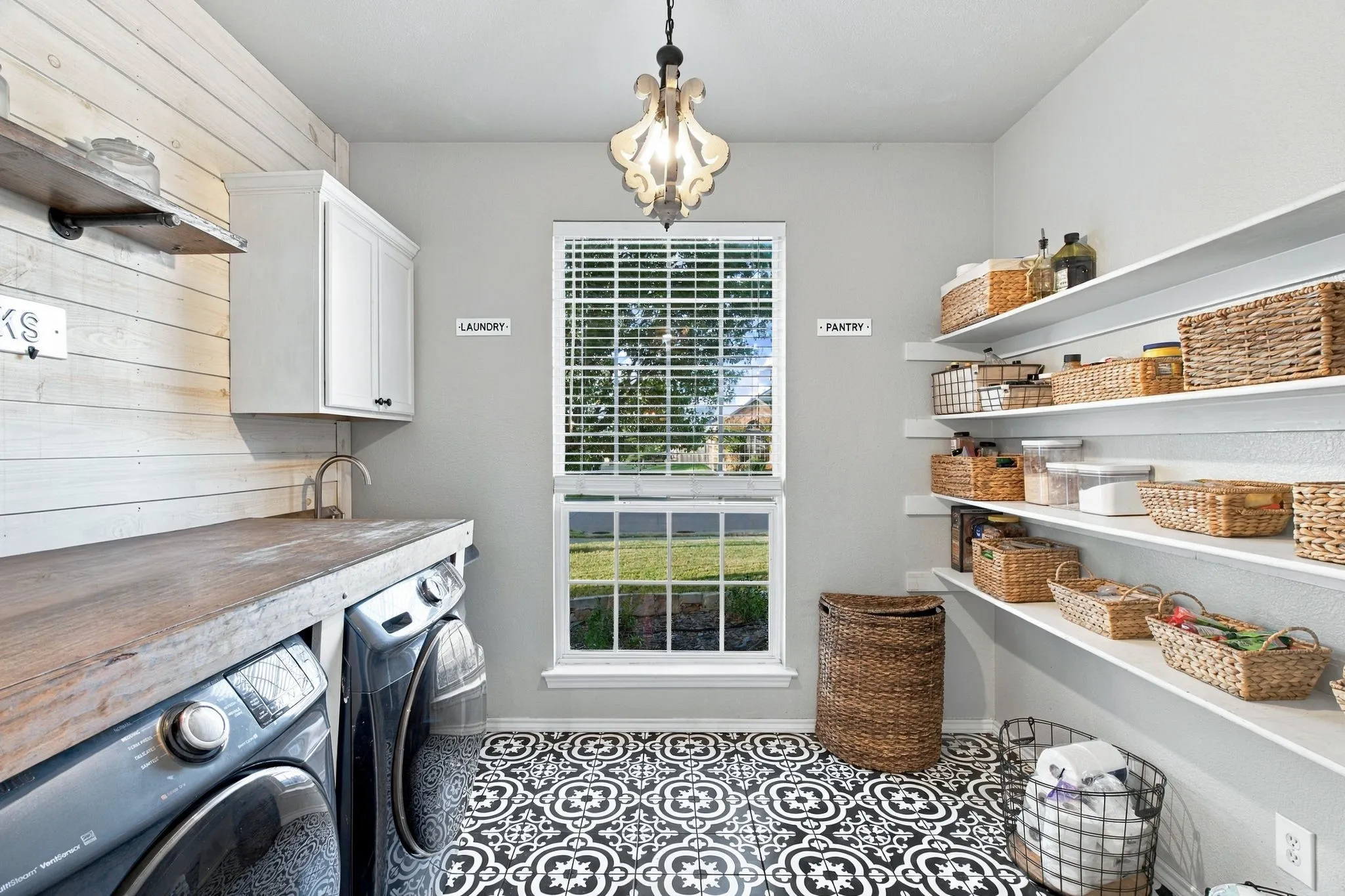 Utility room featuring decorative patterned floor tile, custom wall-mounted shelving, wood-finish countertop, plank-style wall detailing, and an overhead pendant light fixture