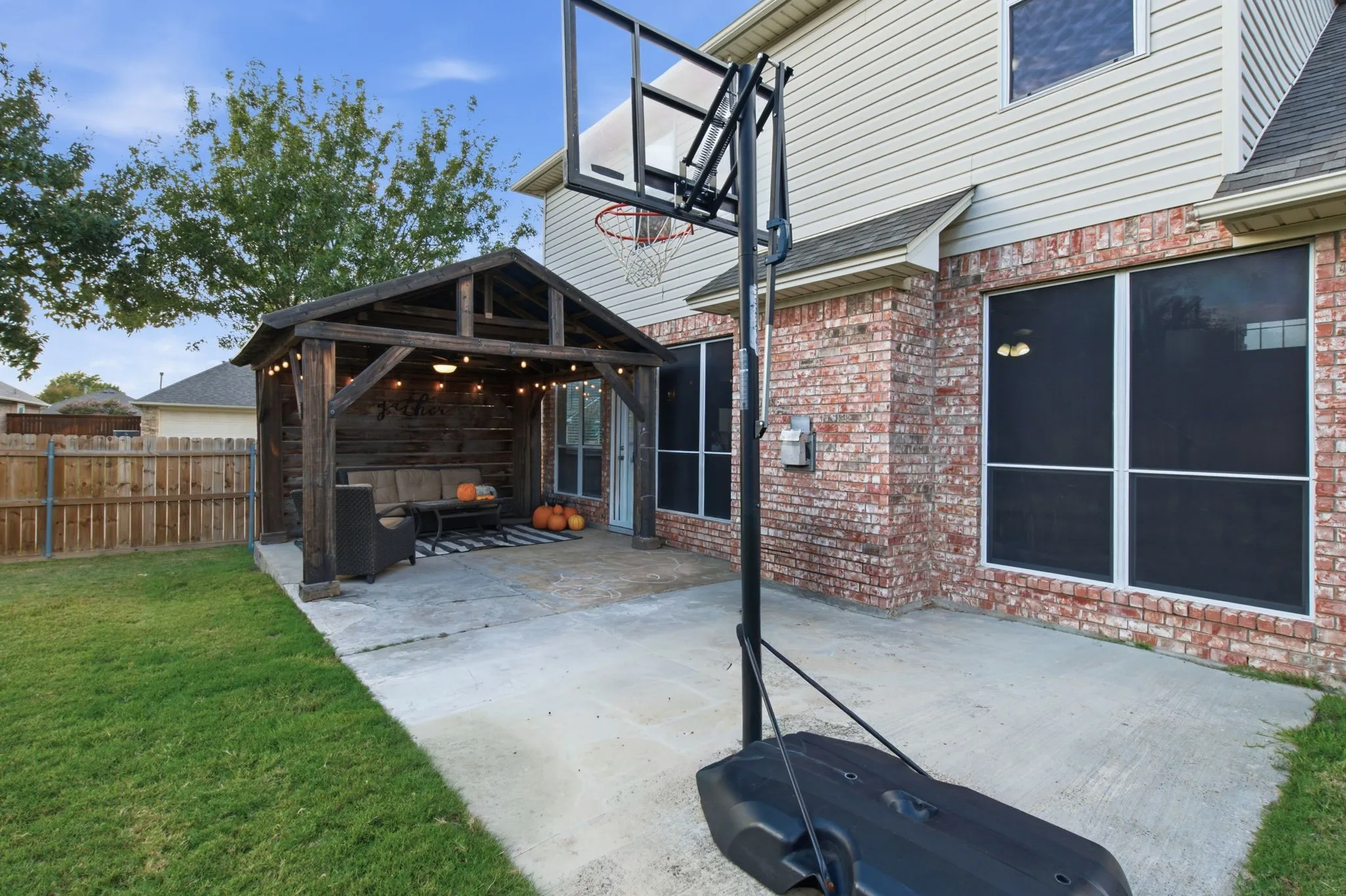 Backyard featuring a concrete patio, wood-frame covered pavilion, brick and siding exterior, and wood-panel fencing