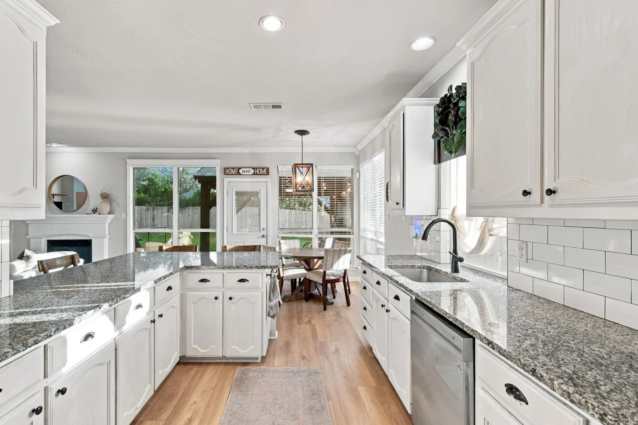 Kitchen featuring white shaker-style cabinetry, speckled stone countertops, a subway tile backsplash, stainless steel dishwasher, and wood-finish flooring