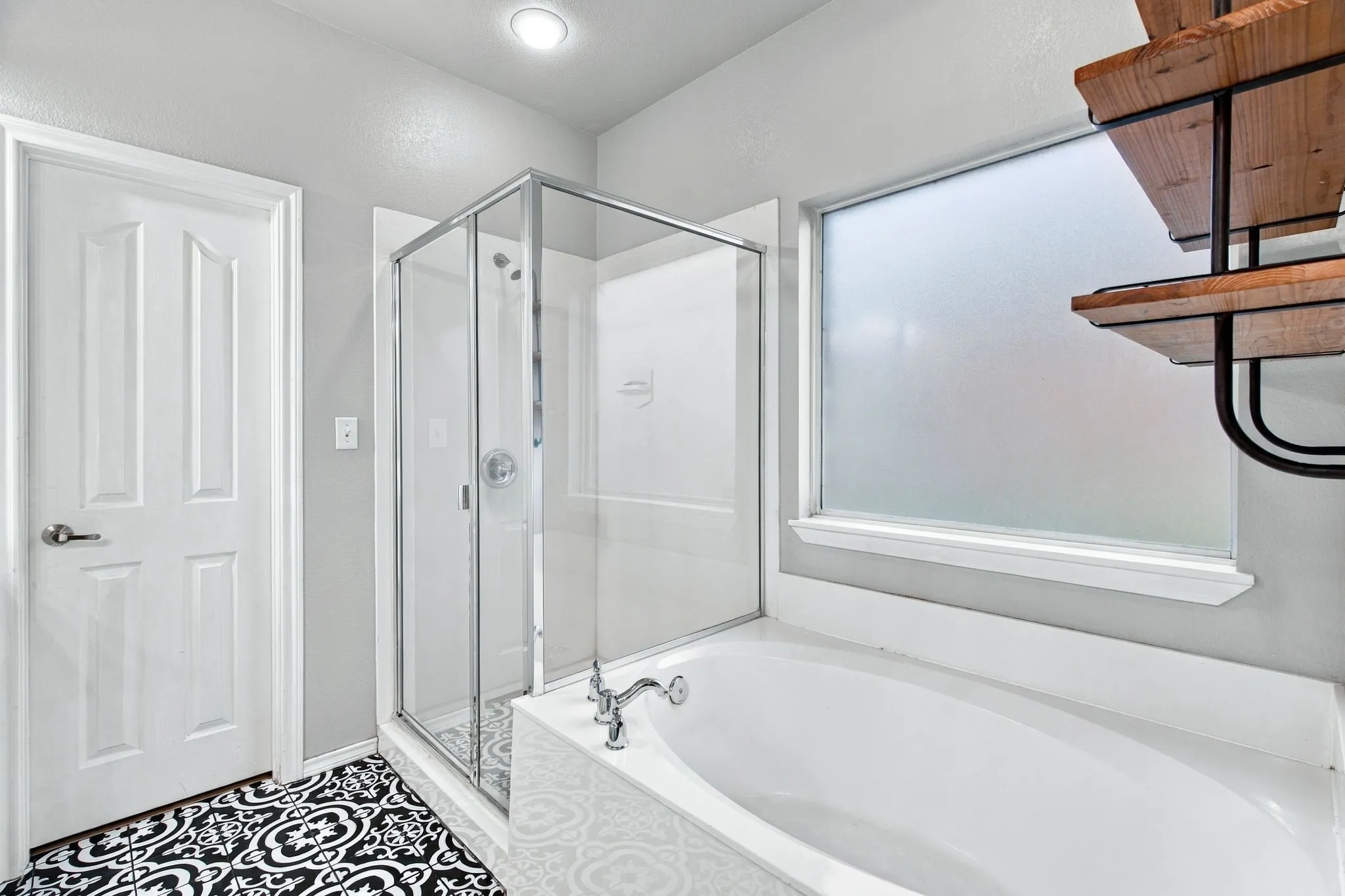 Bathroom featuring a glass-enclosed shower, a deep soaking tub, patterned floor tile, and built-in metal and wood-finish shelving