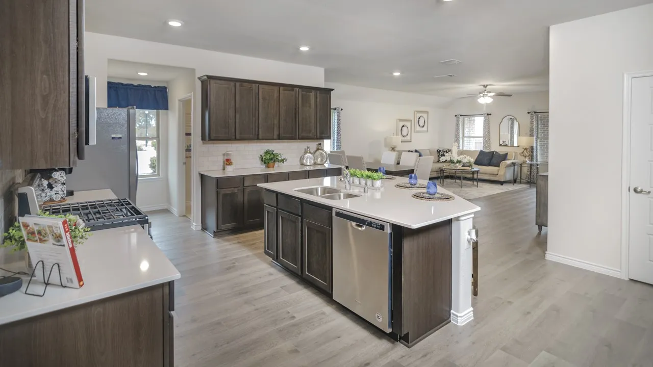 Contemporary kitchen featuring wood-finish cabinetry, light-toned countertops, stainless steel appliances, and a central island with an integrated sink