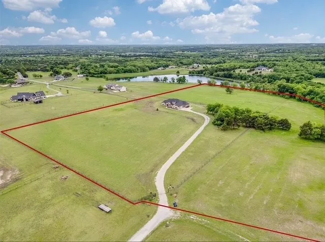 Expansive acreage featuring perimeter fencing, mature tree clusters, a long gravel driveway, and open pastureland