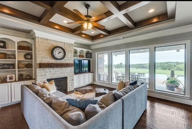 Coffered ceiling with exposed wood beams, stone-faced fireplace with a wood mantel, built-in cabinetry, and expansive windows