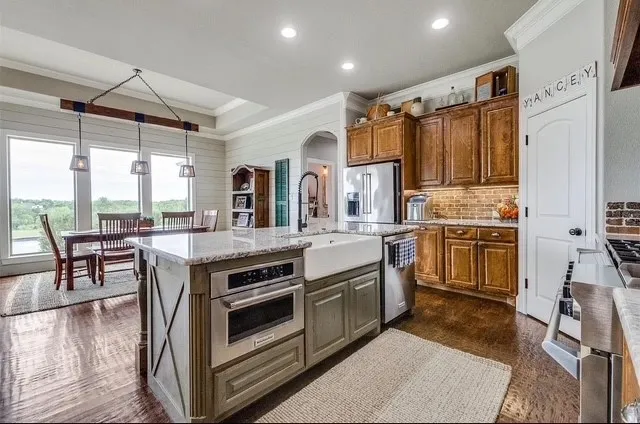 Kitchen featuring an island with a built-in microwave and apron-front sink, wood cabinetry, stone countertops, and recessed lighting