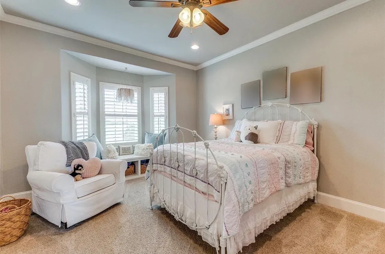 Bedroom featuring neutral wall paint, carpeted flooring, a recessed window nook with integrated bench seating, plantation shutters, and a ceiling fan with multi-light fixture